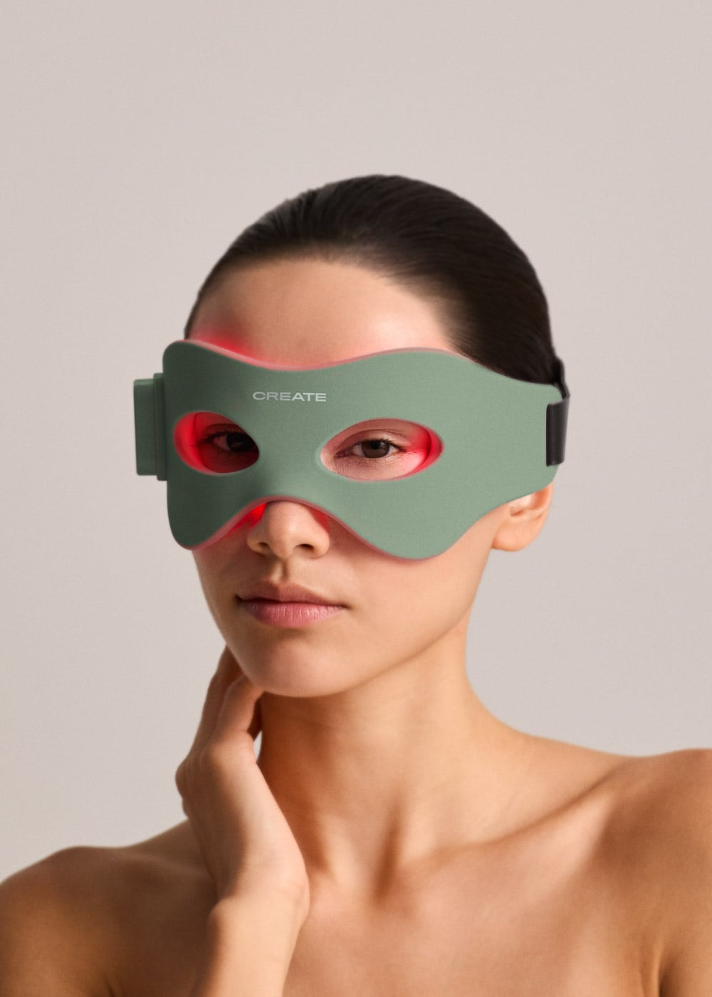 Una mujer con cabello oscuro lleva una máscara de ojos LED verde con luces rojas sobre un fondo neutral.