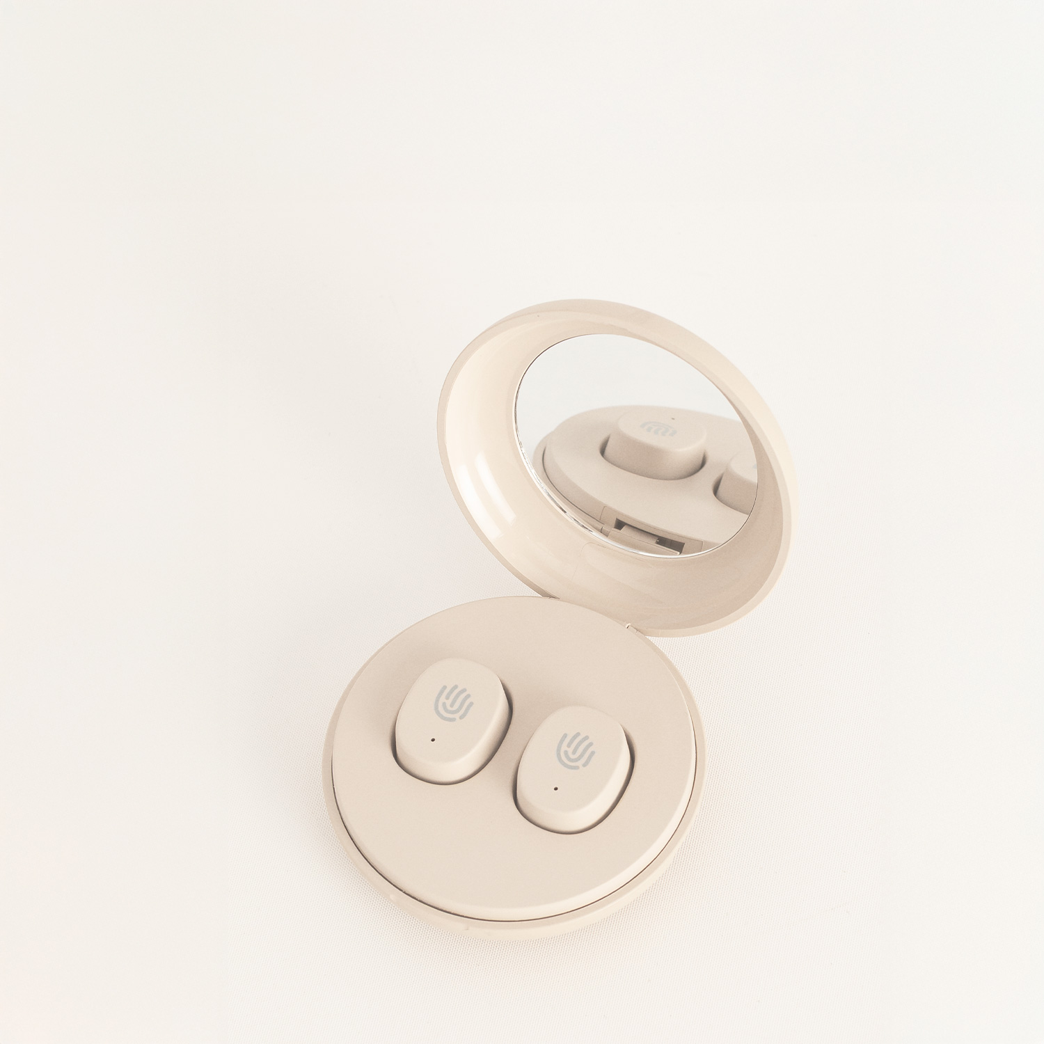 Estuche de auriculares redondo y beige con espejo abierto y dos auriculares dentro, sobre fondo claro.