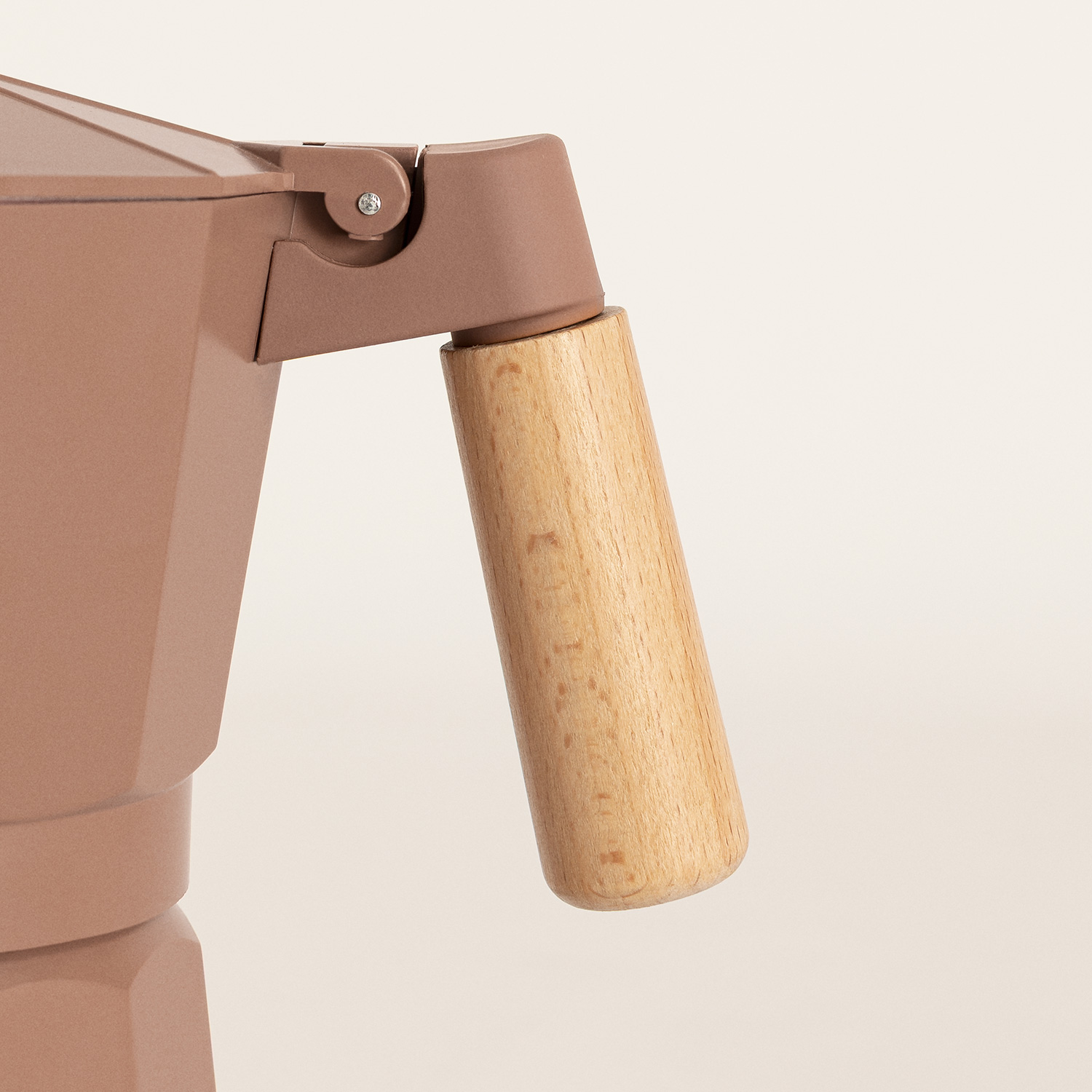 Primer plano de una cafetera moka beige con mango de madera sobre fondo claro.