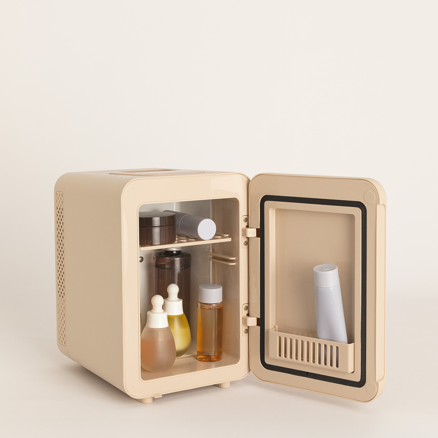 Una mini nevera beige abierta sobre una superficie blanca contiene varios frascos cosméticos.