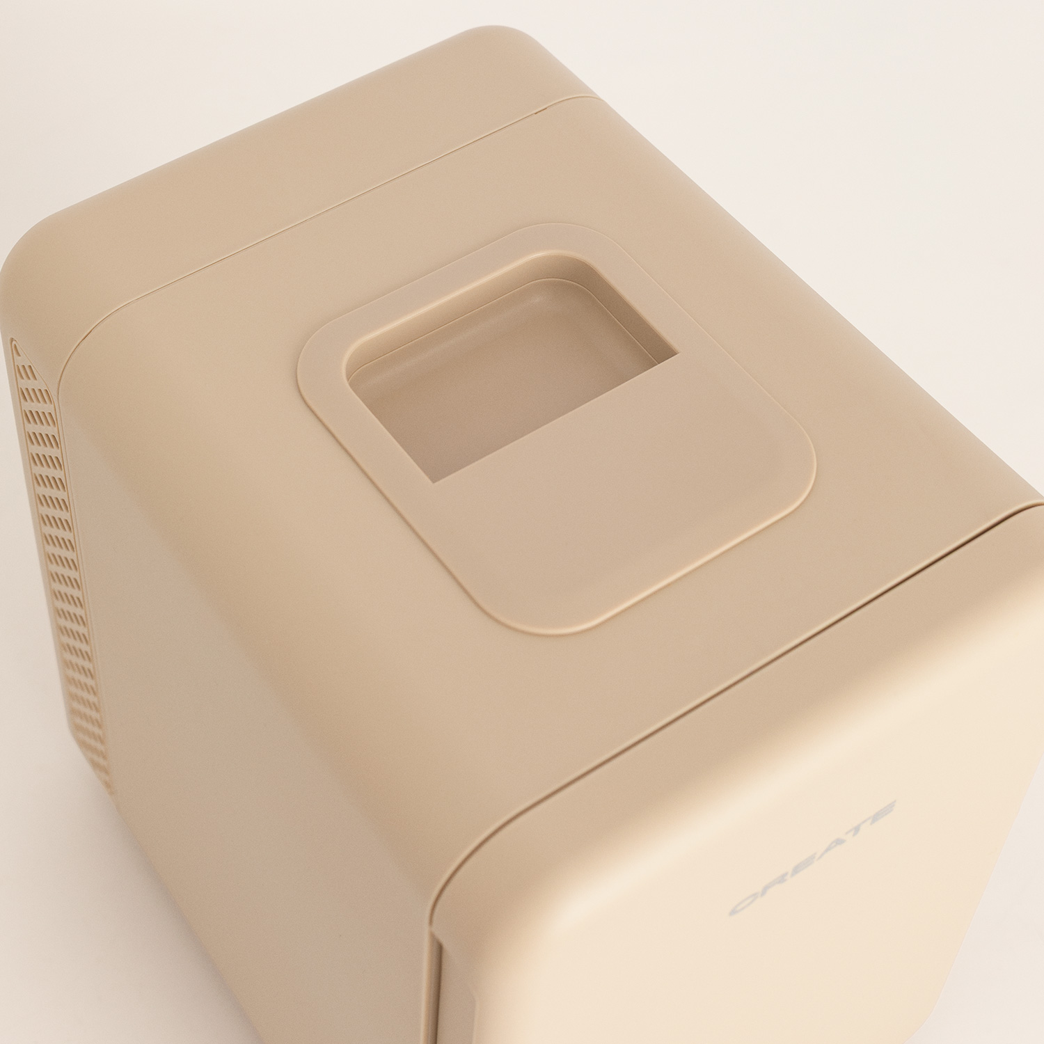 Una mini nevera beige sobre una superficie clara, vista desde arriba, con asa superior y ranuras de ventilación.