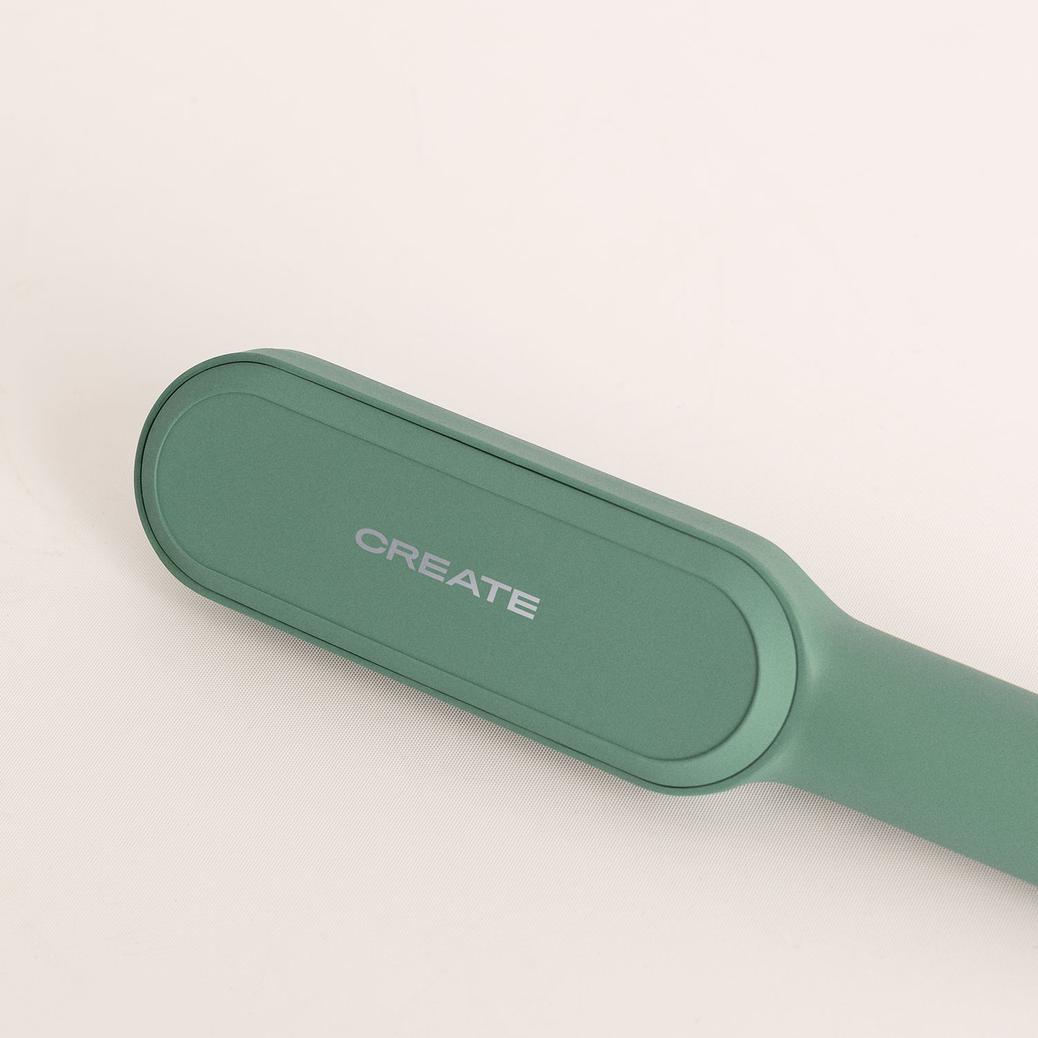 Una plancha de pelo verde mate con el texto CREATE sobre una superficie clara.