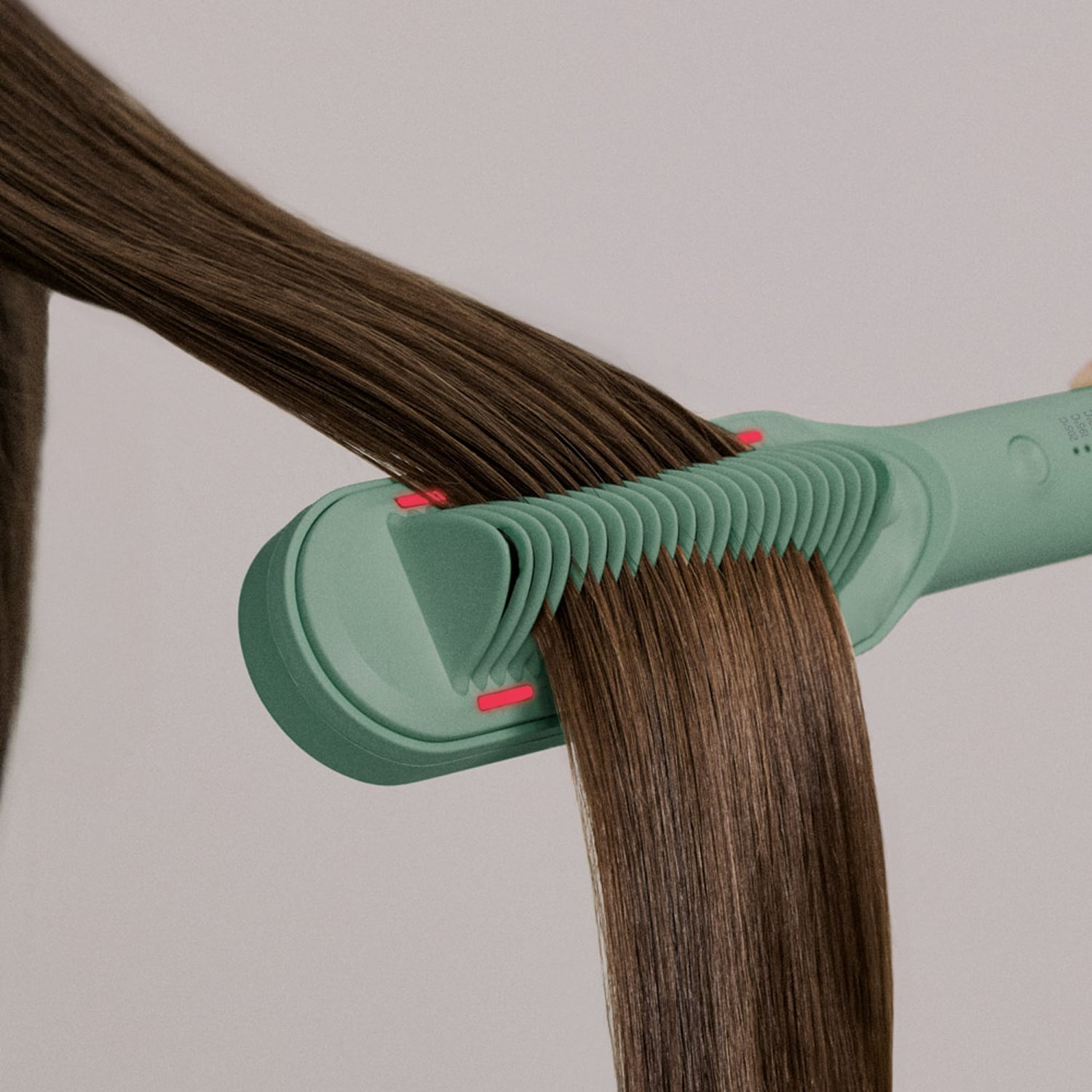 Una herramienta de peinado verde menta alisa una sección de cabello castaño largo.