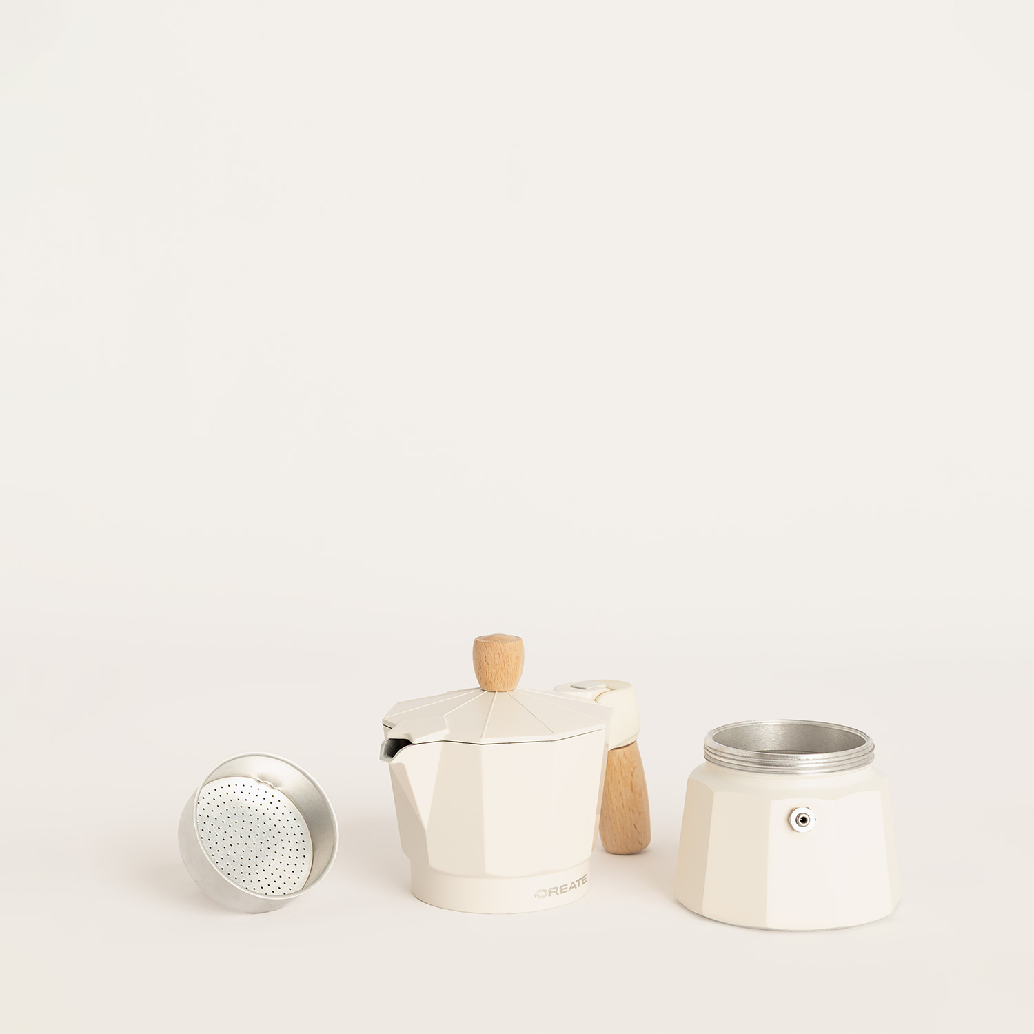 Una cafetera moka blanca desmontada con filtro y detalles de madera sobre fondo claro.