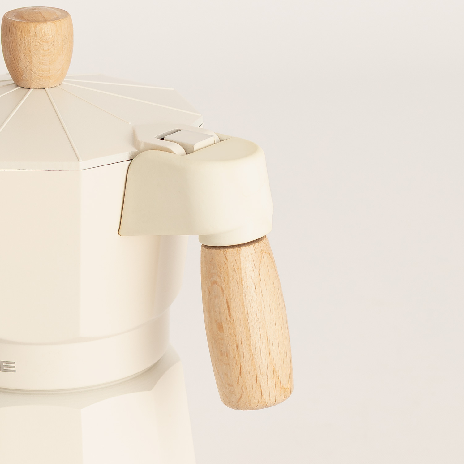 Primer plano de una cafetera moka color crema con pomo y mango de madera sobre fondo blanco.