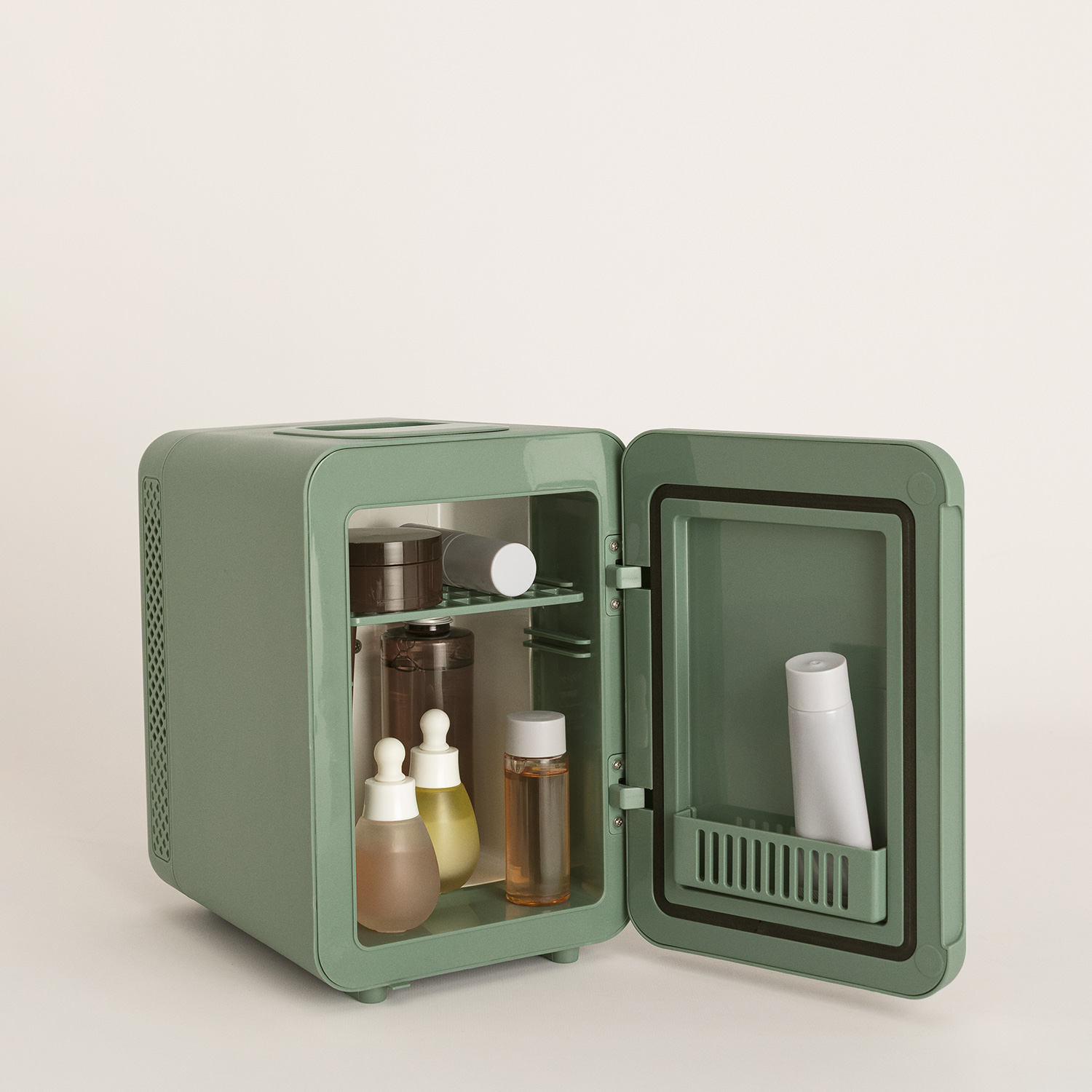 Una mini nevera verde pastel abierta sobre una superficie blanca, llena de botellas de cuidado de la piel.