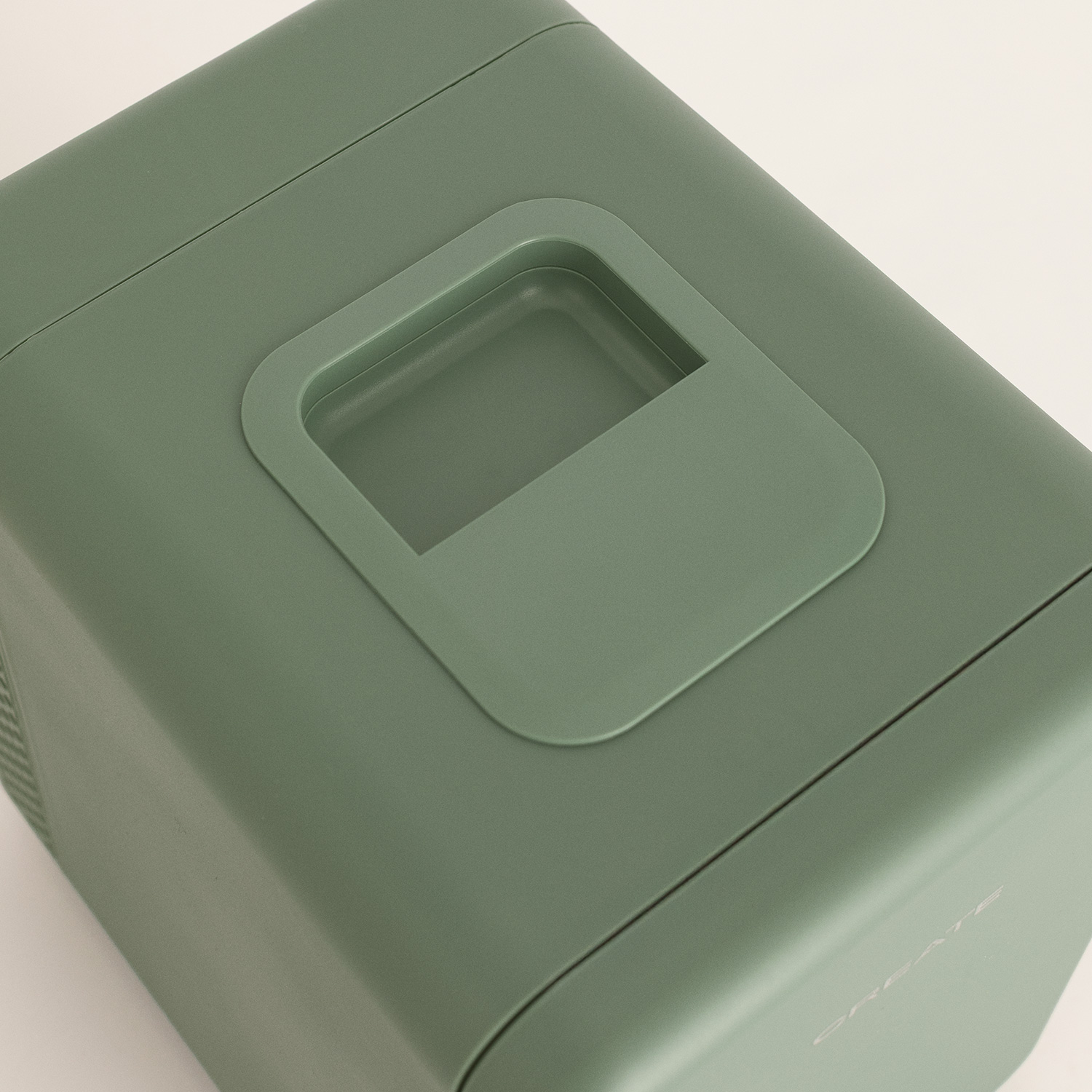 Una máquina de hielo portátil verde mate con un asa integrada en la parte superior sobre fondo claro.