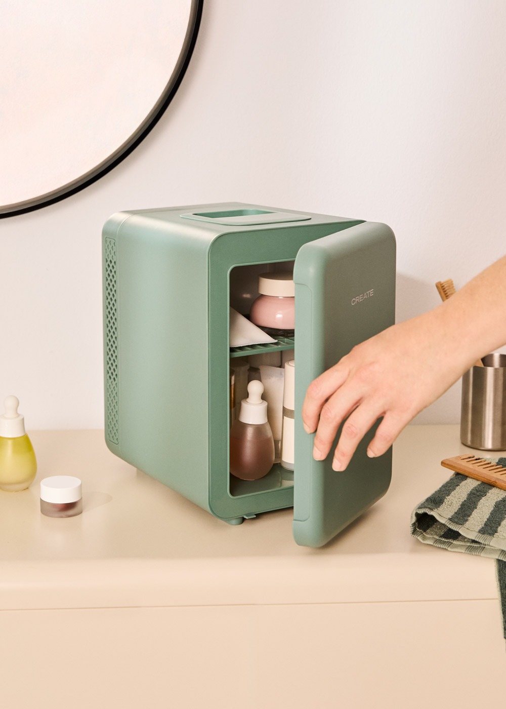 Una mano abre un pequeño refrigerador cosmético verde menta lleno de productos para el cuidado de la piel.