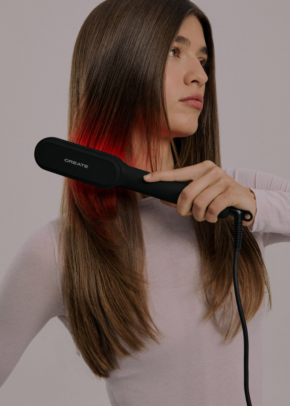 Una mujer usa una herramienta de peinado Create negra en su cabello castaño largo y liso con reflejos rojos.