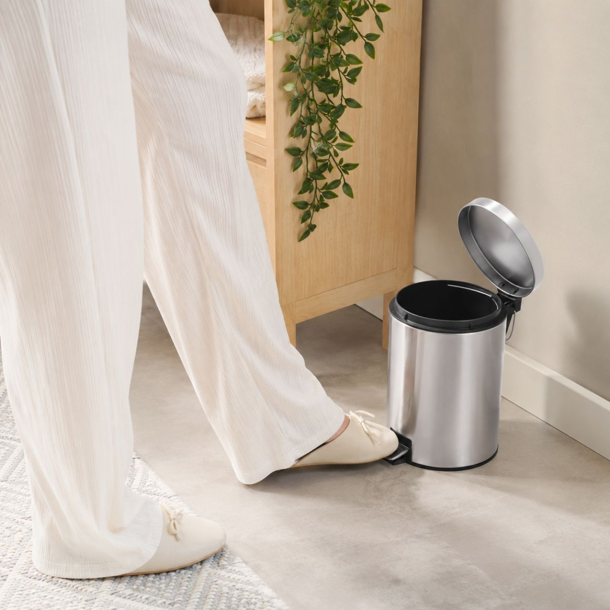 Une personne en pantalon blanc appuie sur la pédale d'une petite poubelle en inox.