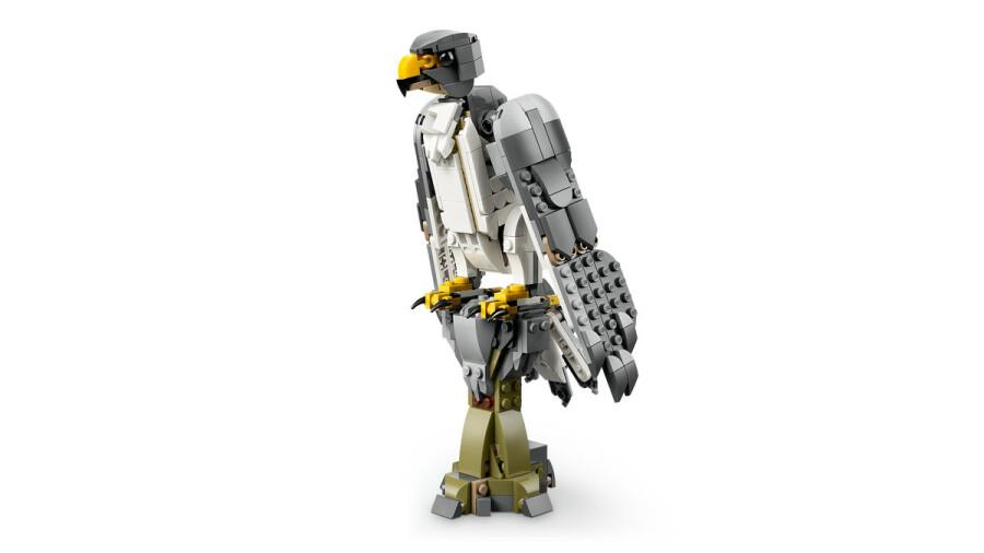 Gri ve beyaz tüylü, sarı gaga ve pençeli Lego şahin modeli, yeşil bir Lego ağaç kütüğü üzerinde duruyor.