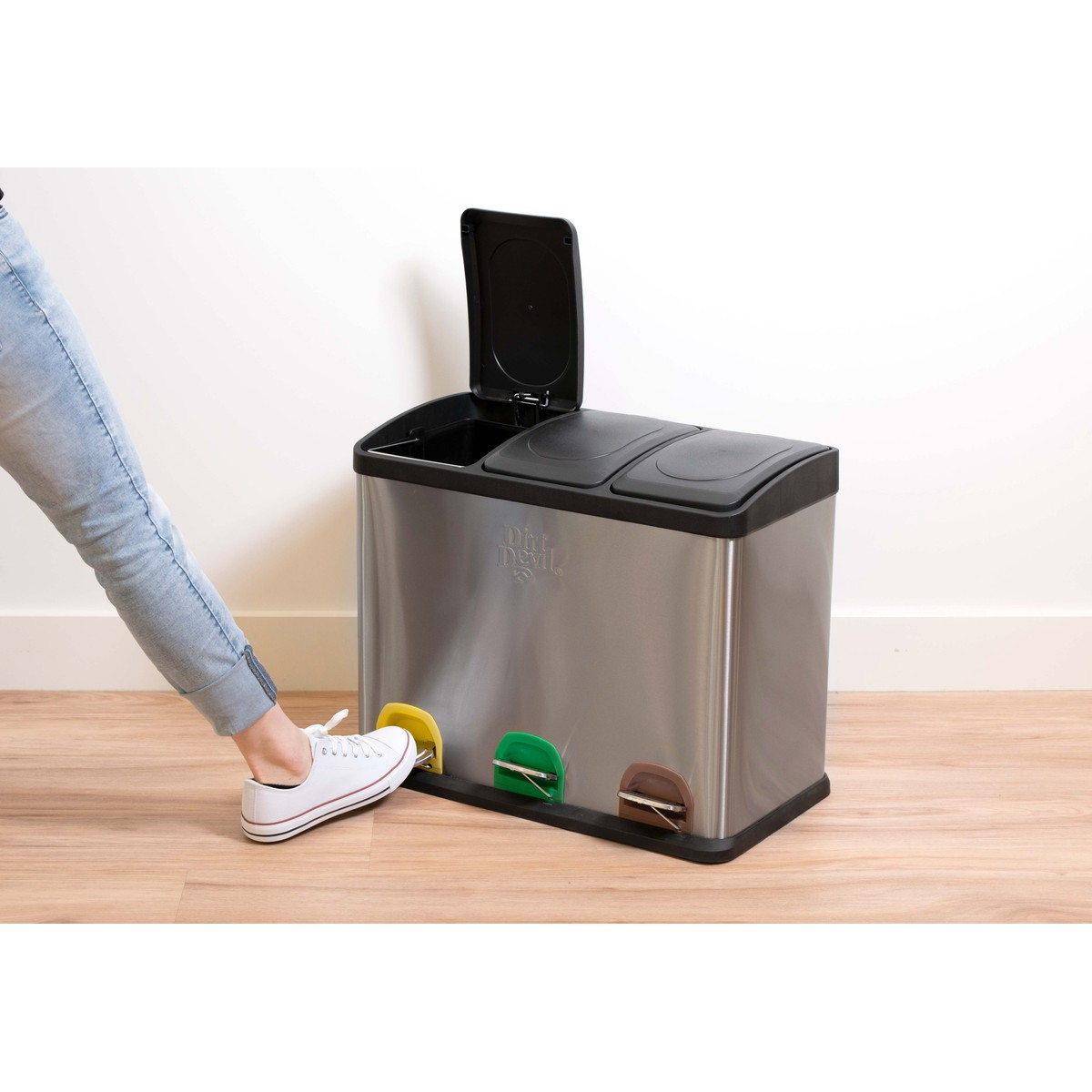 Un pied appuie sur la pédale jaune pour ouvrir le couvercle d'une poubelle en inox.