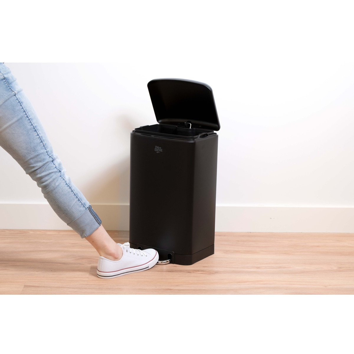 Une personne appuie sur la pédale d'une poubelle noire avec une basket blanche.