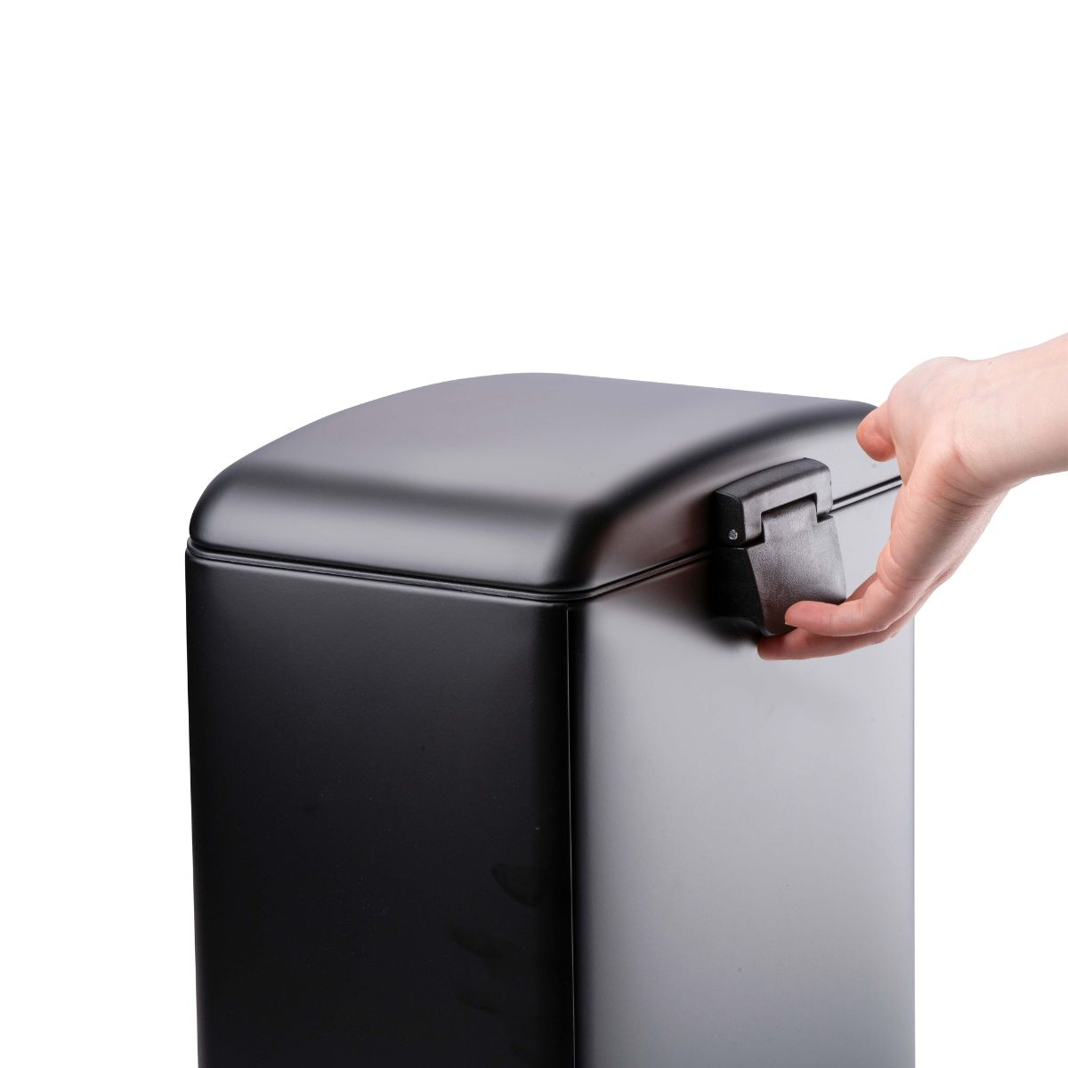A hand opens the lid of a black trash can against a white background.
