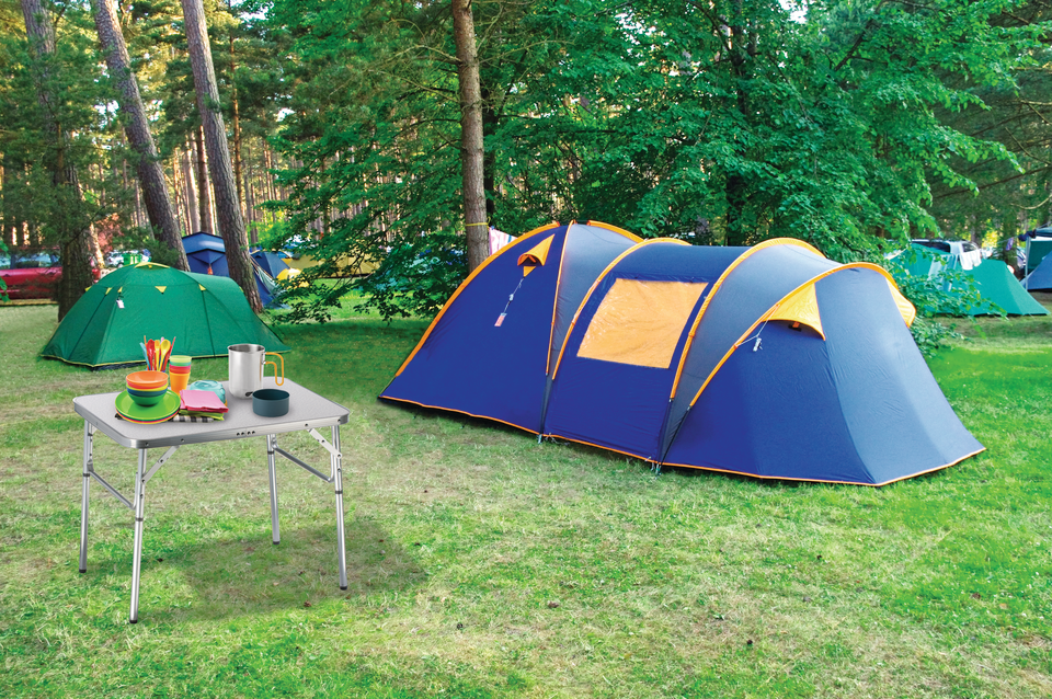 Une tente bleue et une table pliante avec de la vaisselle se trouvent dans un camping.