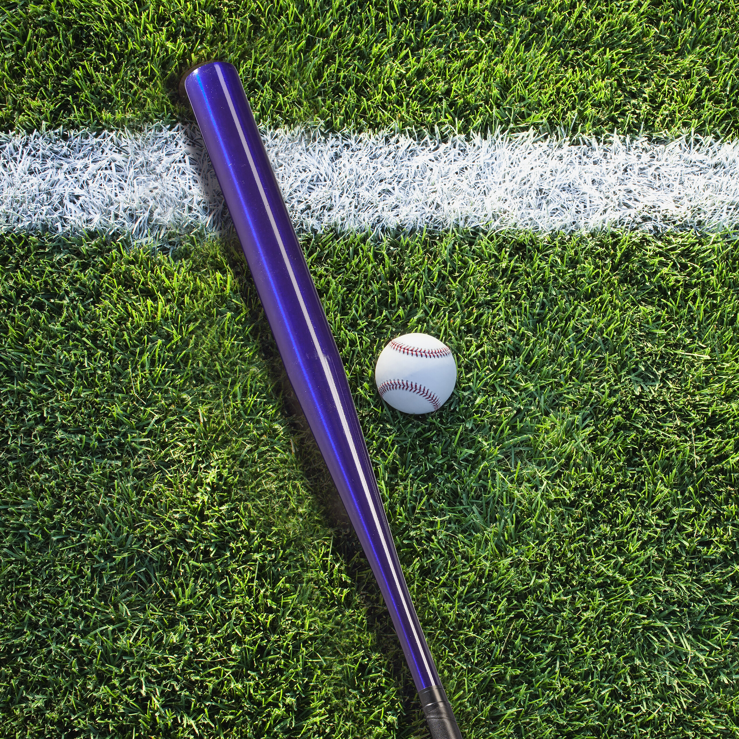 Ein blauer Baseballschläger und ein Baseball liegen auf grünem Rasen neben einer weißen Linienmarkierung.