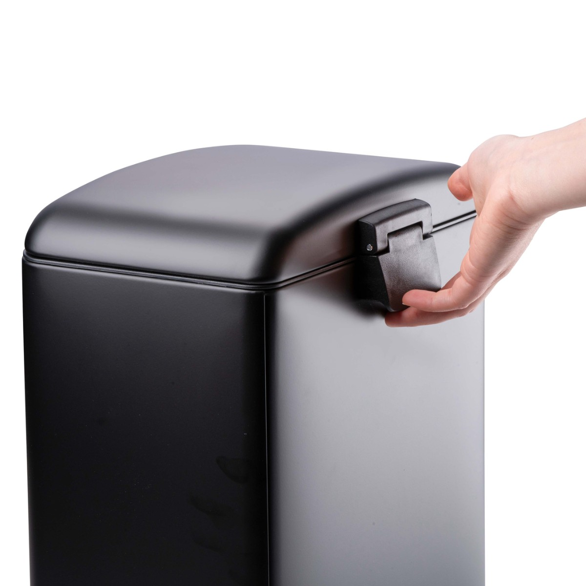Une main ouvre le couvercle noir d'une poubelle rectangulaire noir mat sur fond blanc.