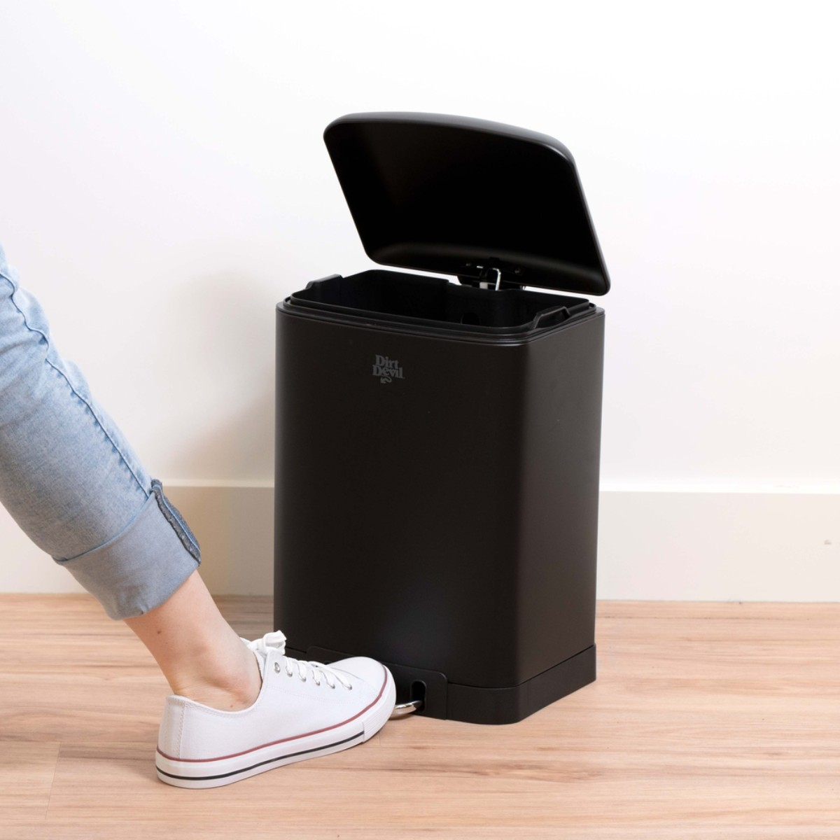 Un pied dans une sneaker blanche appuie sur la pédale d'une poubelle noire.