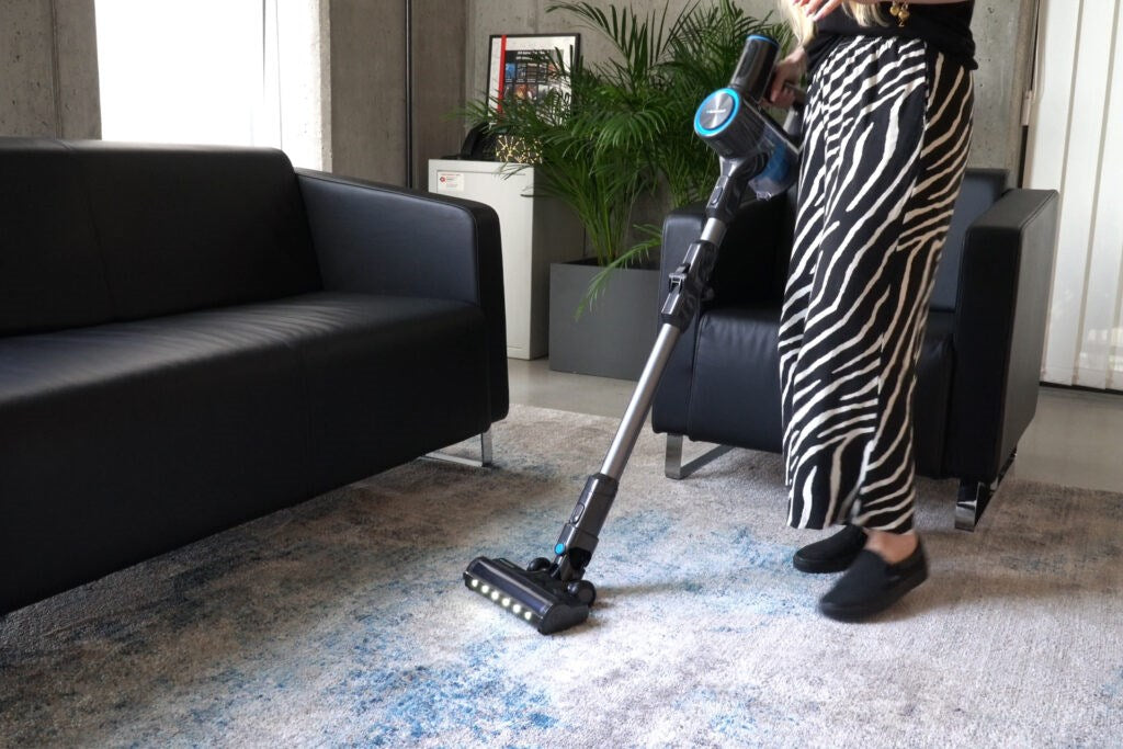 Eine Person in Zebradruck-Hose saugt einen gemusterten Teppich in einem modernen Wohnzimmer.