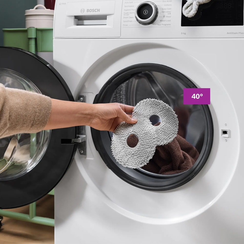 Eine Hand legt graue Wischpads in die Trommel einer weißen Bosch-Waschmaschine.