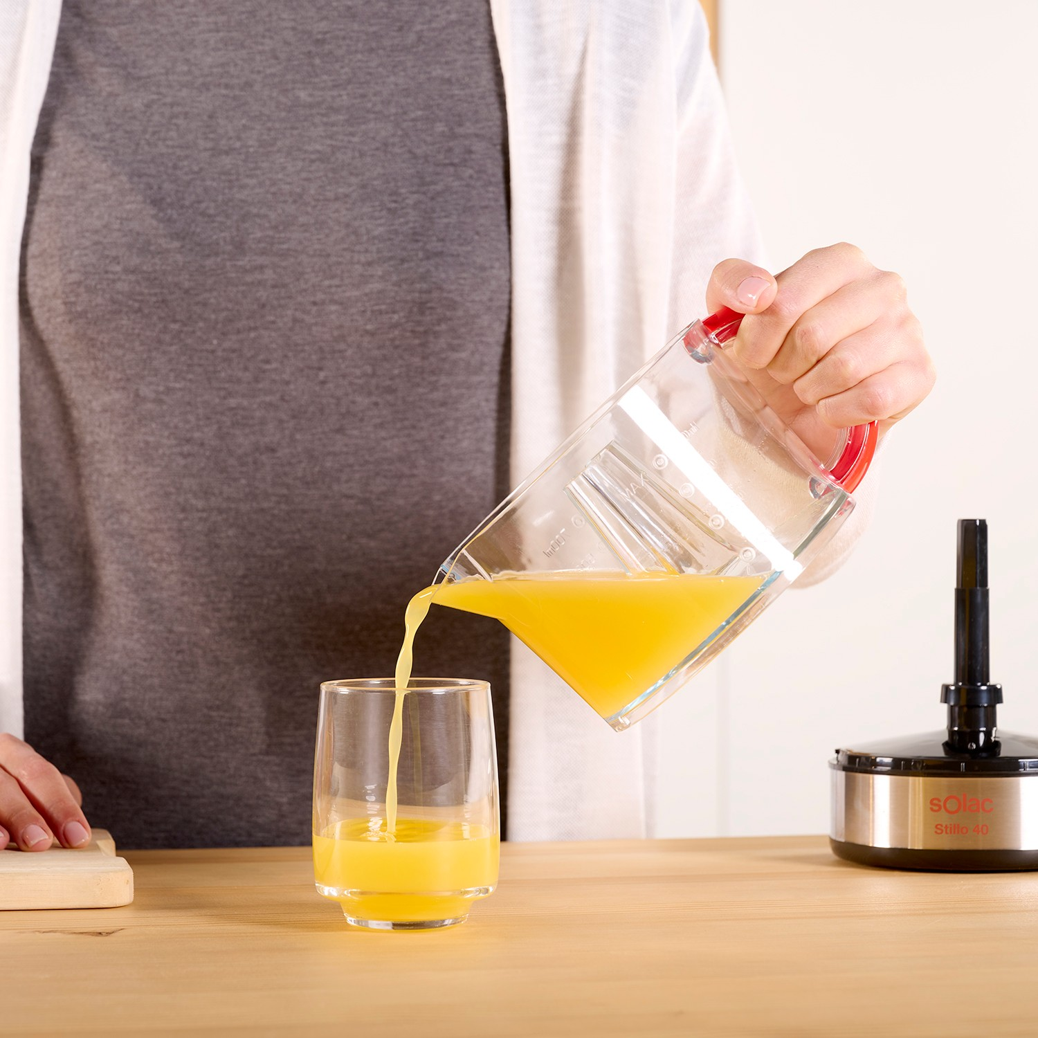Una persona vierte jugo de naranja de un recipiente transparente en un vaso sobre una mesa de madera.