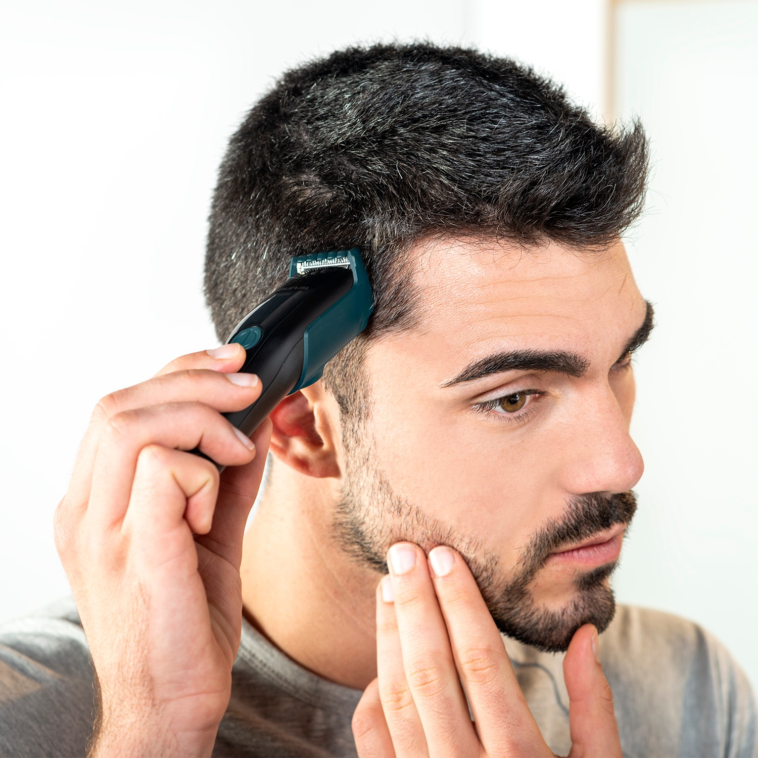Un hombre con pelo corto y oscuro se recorta el cabello de un lado con una cortadora negra.
