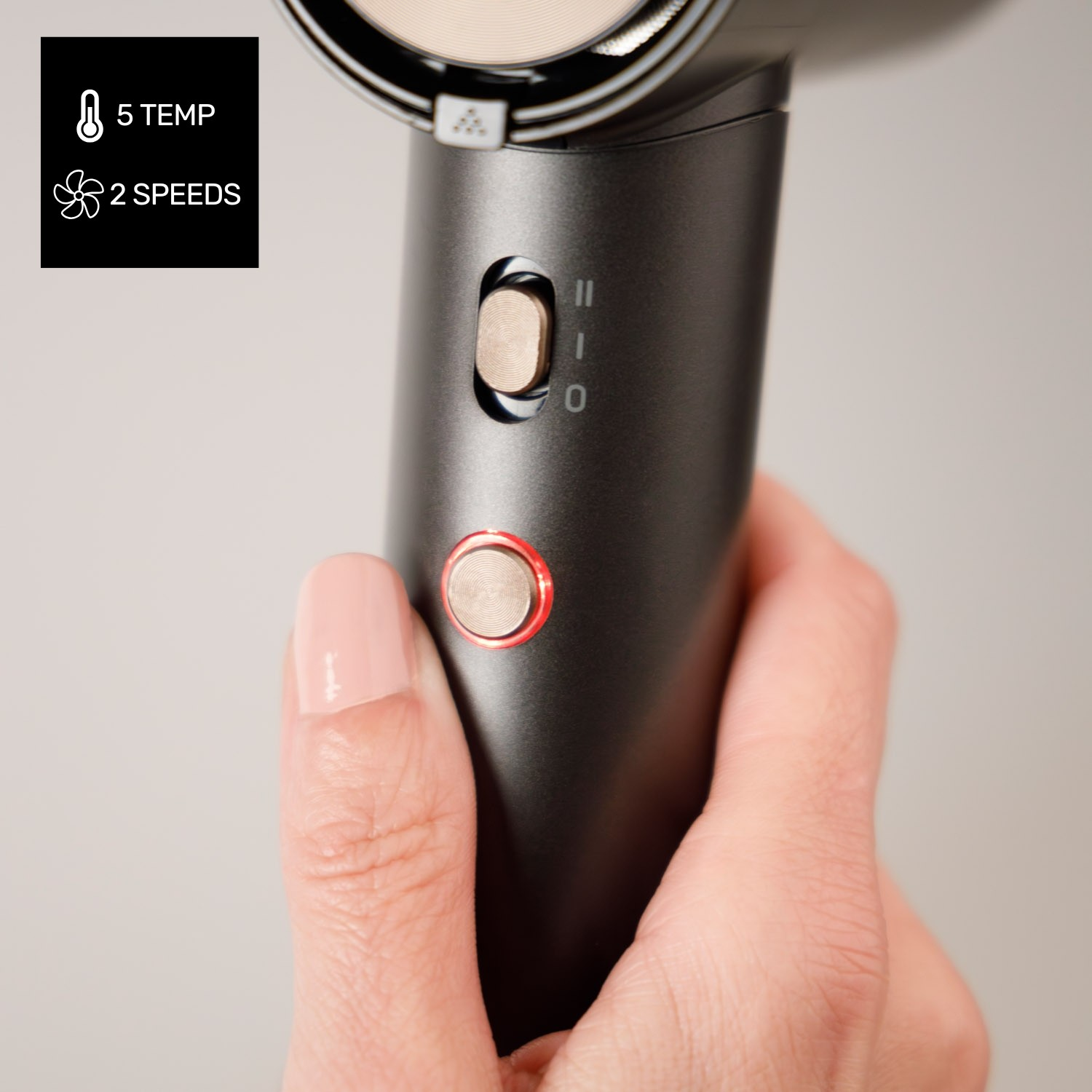 Mano sosteniendo un secador de pelo negro mate con botones plateados y acentos rojos.
