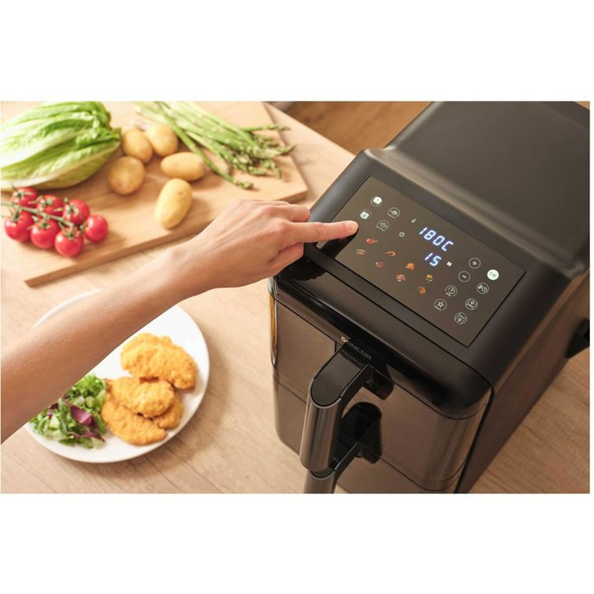 Mano che aziona il display digitale di una friggitrice ad aria nera vicino a verdure fresche.