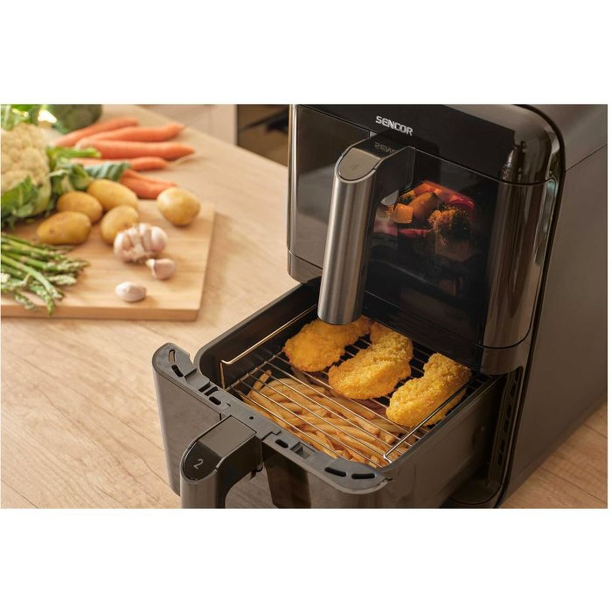 Una friggitrice ad aria nera su un tavolo di legno con il cestello aperto contenente patatine fritte e pollo impanato.