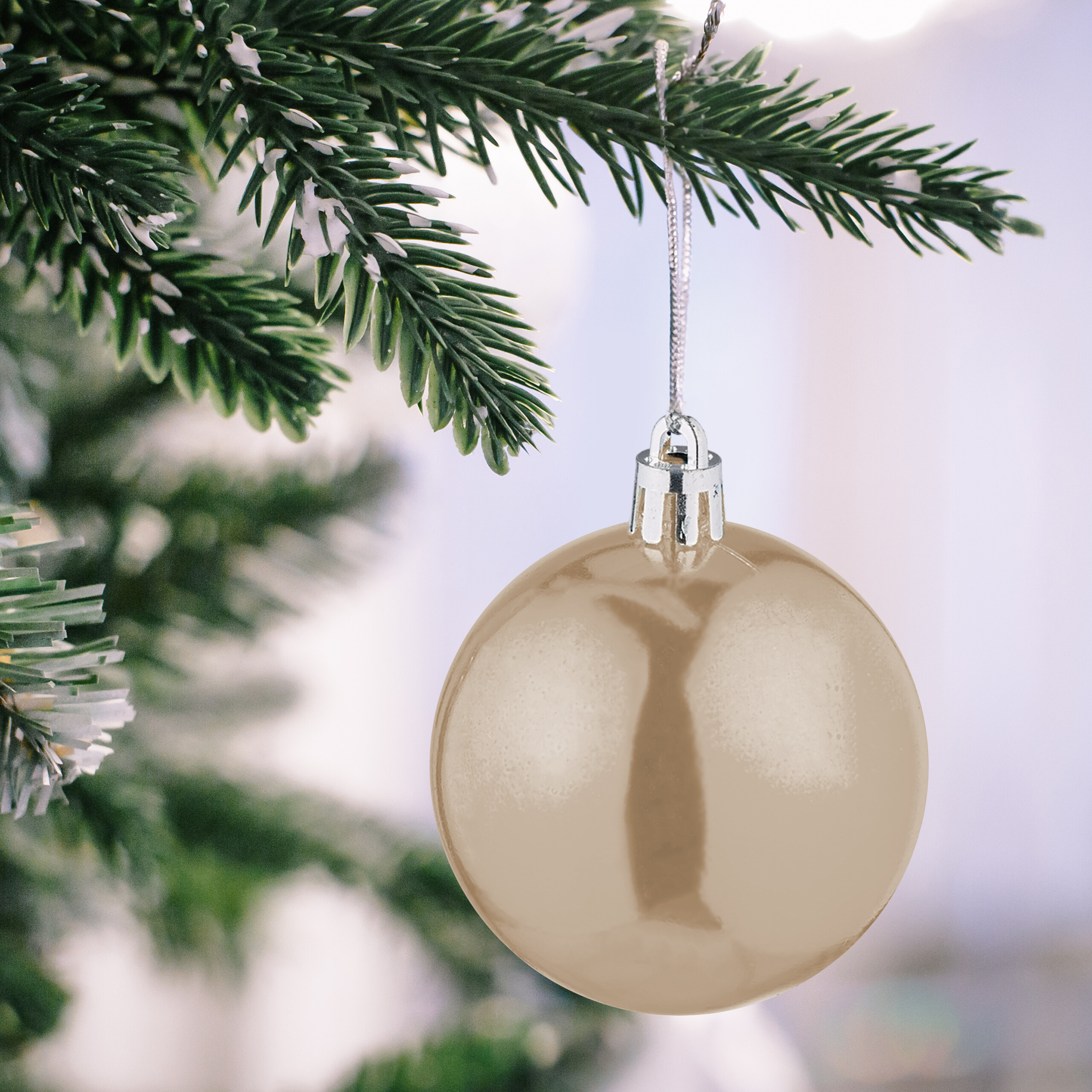 Eine glänzende beige Christbaumkugel hängt an einem schneebedeckten Tannenast.