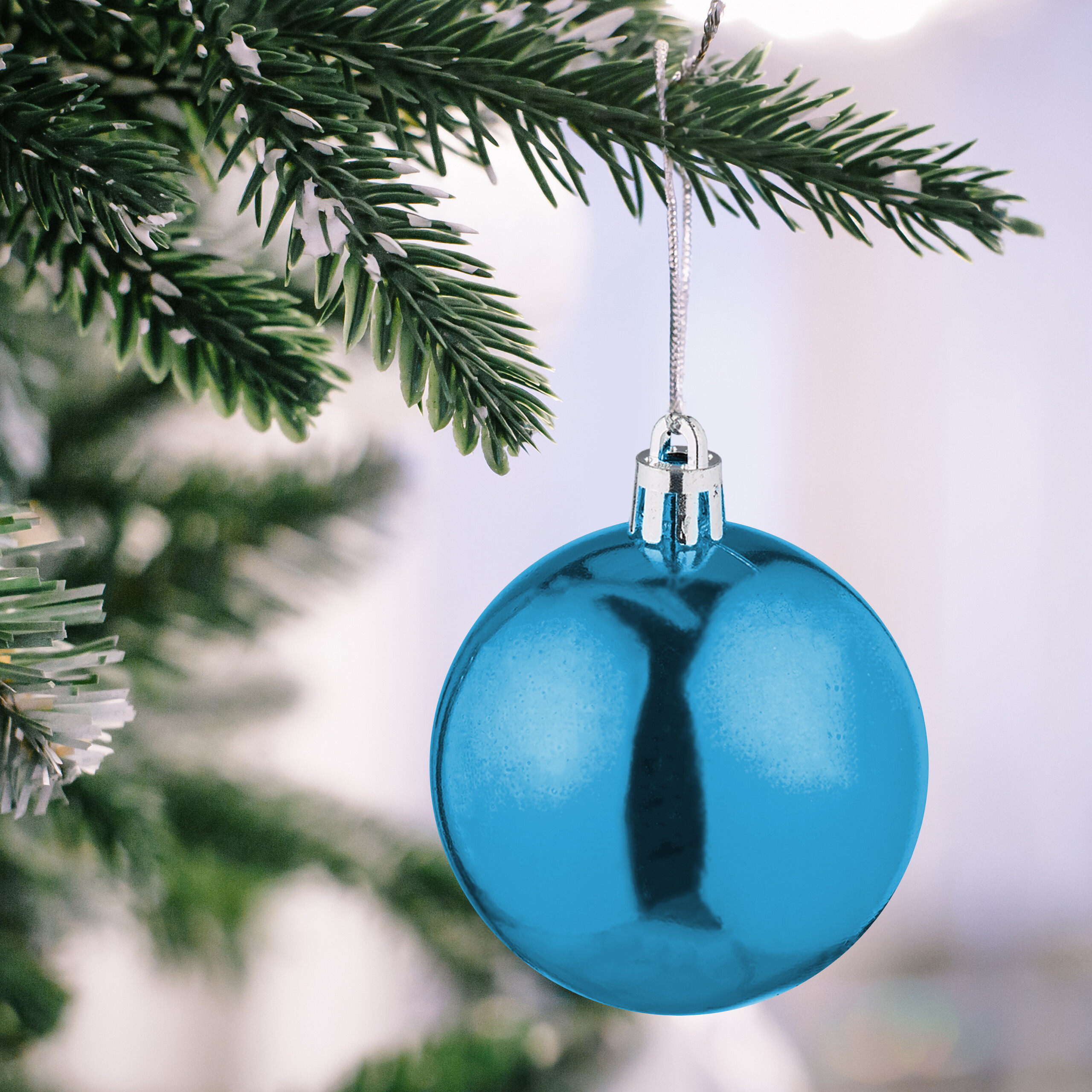 Glänzende blaue Weihnachtskugel hängt an einem verschneiten Tannenzweig.