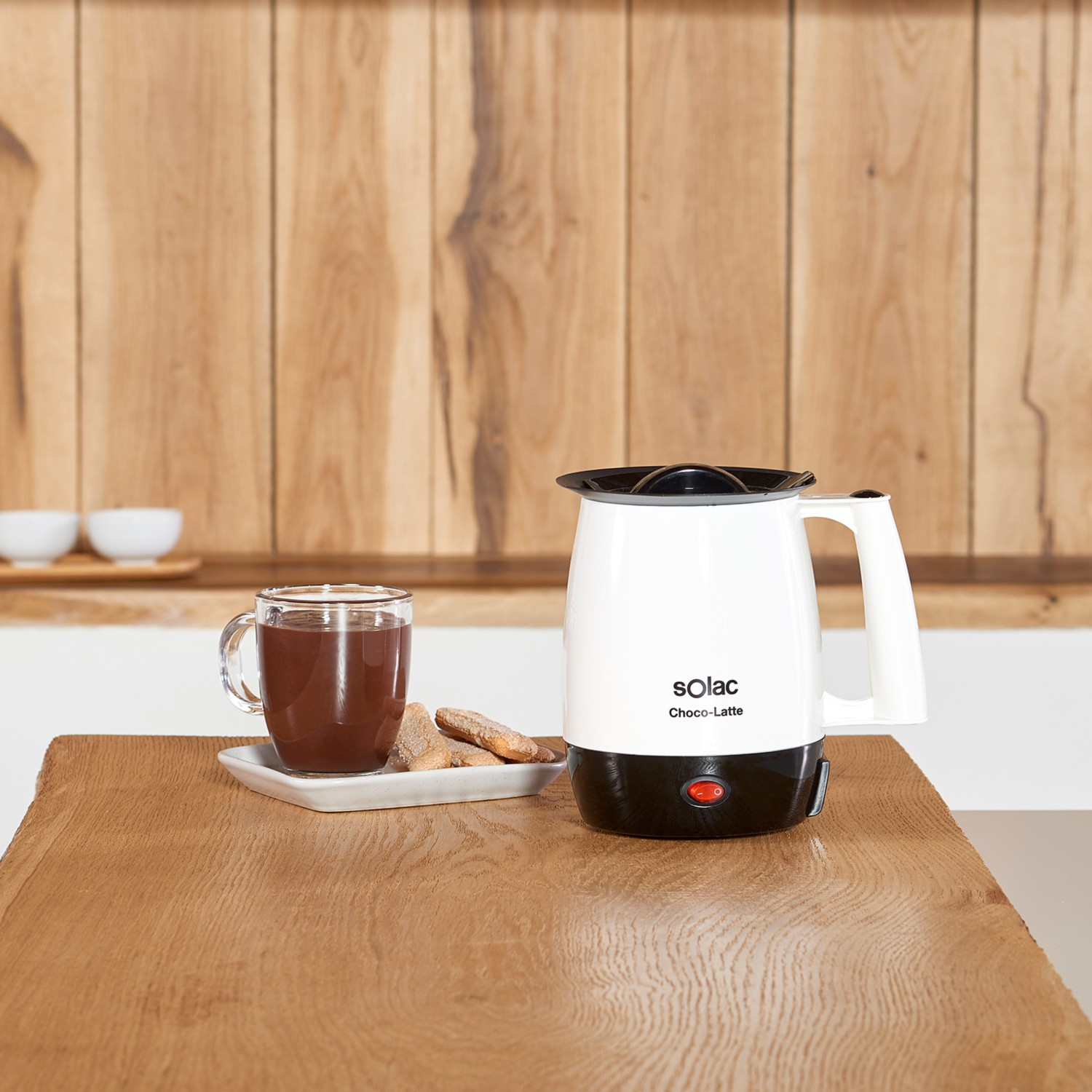 Un espumador de leche Solac Choco-Latte en una mesa de madera con una taza de chocolate caliente y galletas.