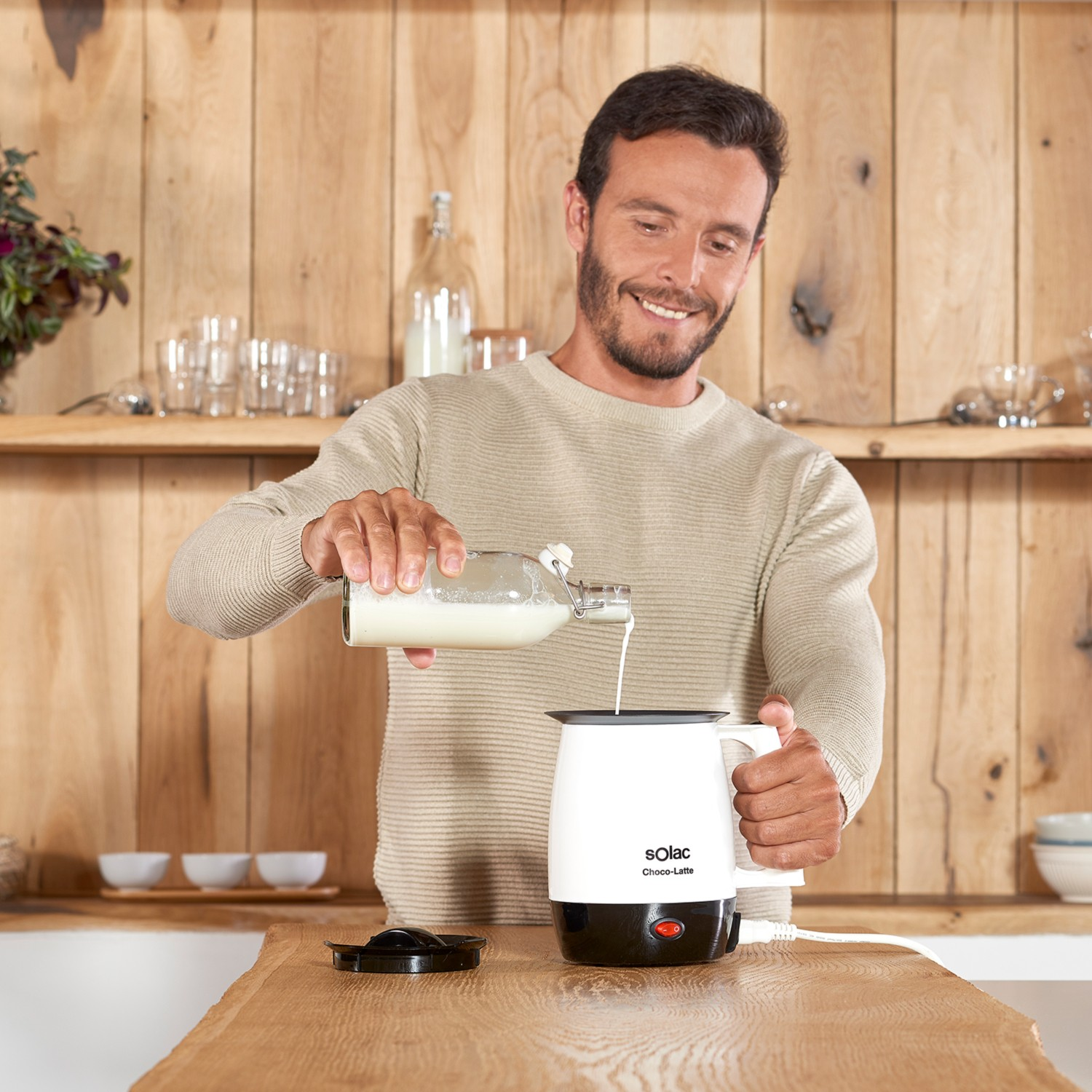 Un hombre vierte leche de una botella de vidrio en un espumador de leche blanco Solac Choco-Latte.