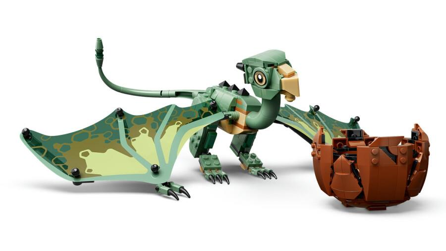 Beyaz arka planda kırık kahverengi bir Lego yumurtasının yanında duran yeşil bir Lego ejderhası.
