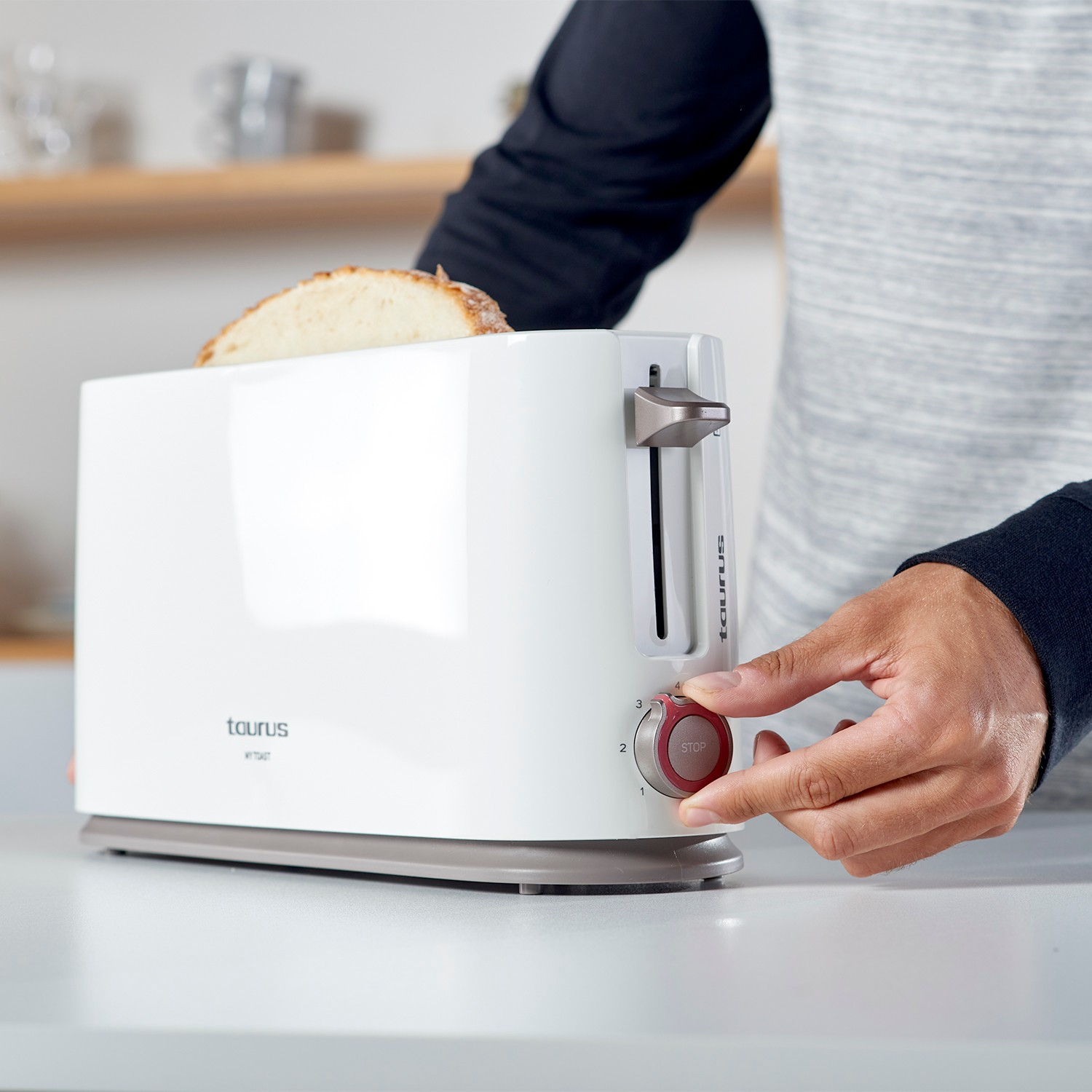 Una persona ajustando la configuración en una tostadora Taurus blanca con una rebanada de pan dentro.