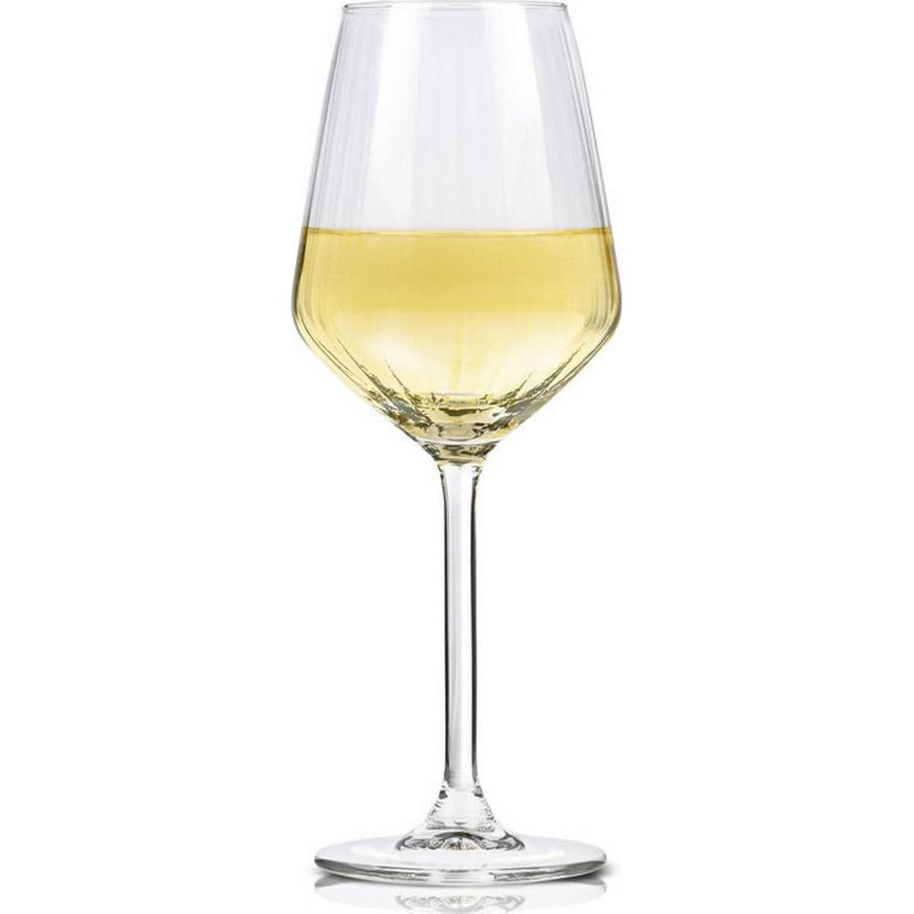 An elegant, ribbed wine glass filled with light white wine stands on a white surface against a white background.