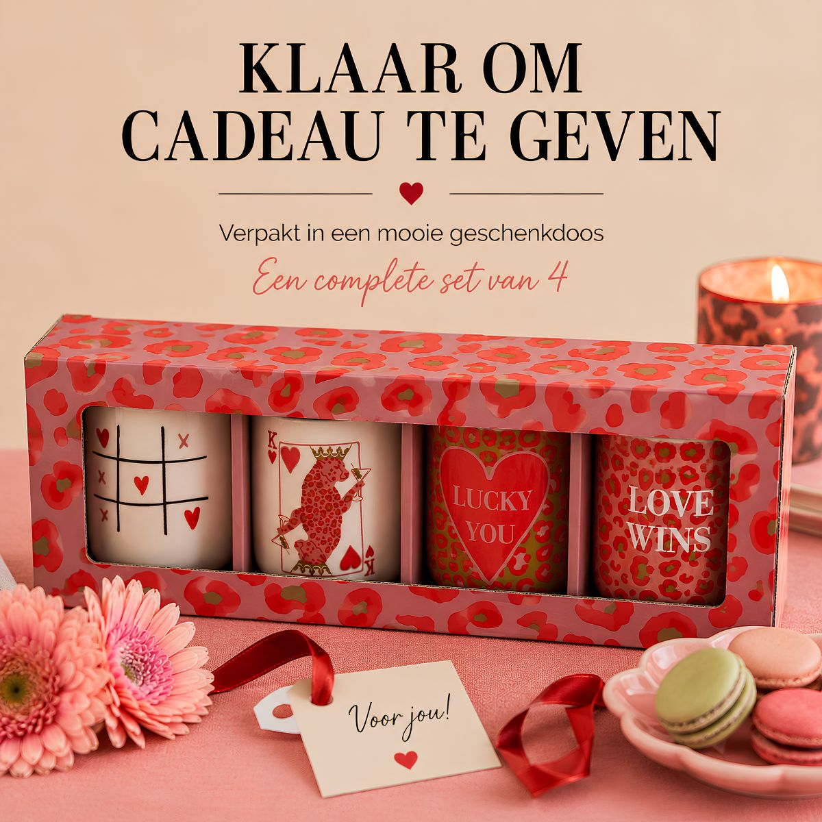 A set of four mugs in a gift box, surrounded by flowers, macarons, and a candle.