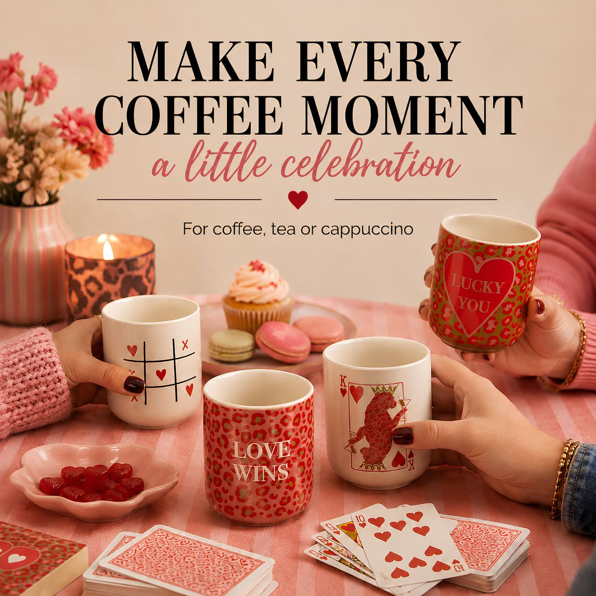 People hold coffee mugs with heart motifs, surrounded by cupcakes, candles, and playing cards on a table.