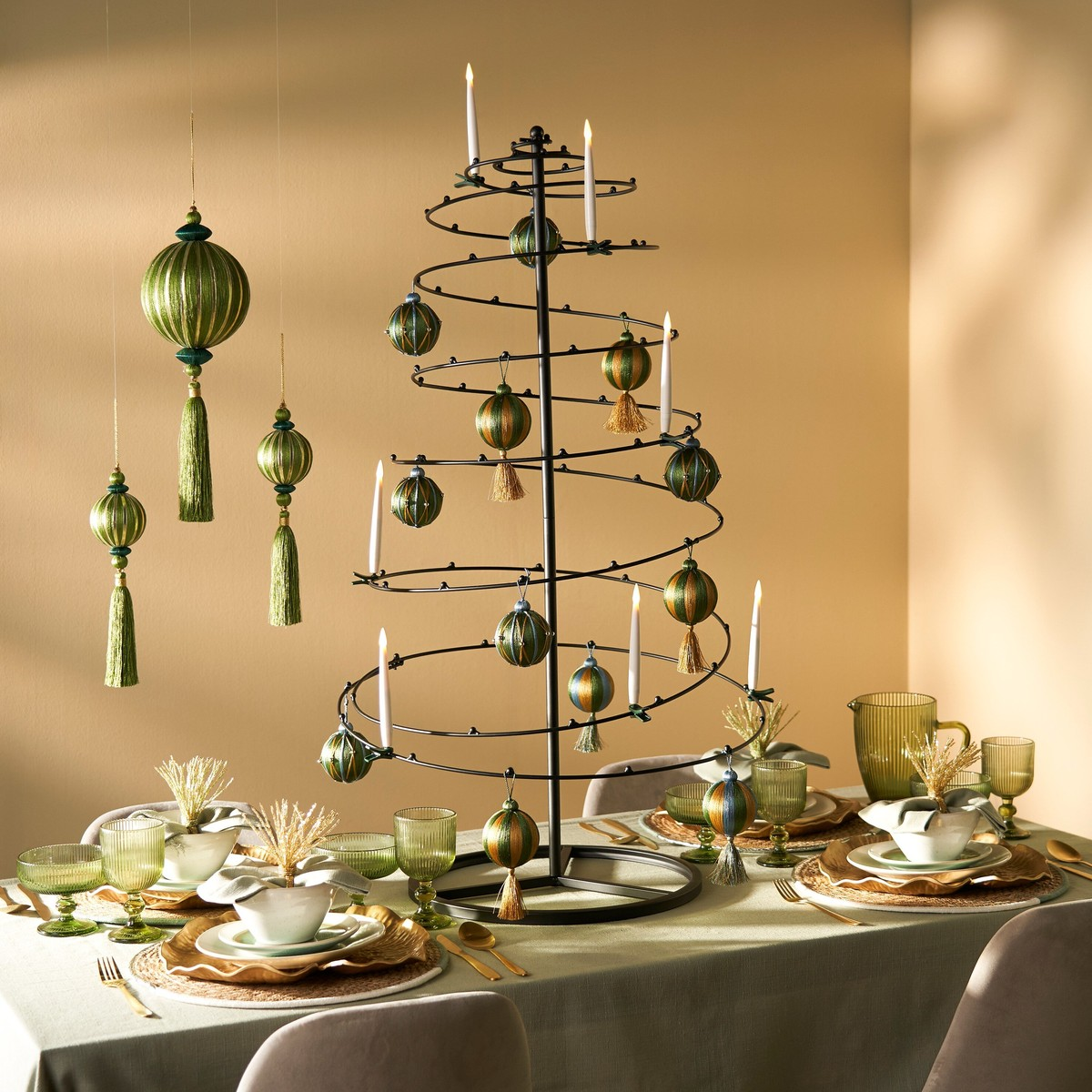 A set dining table with a black spiral Christmas tree centerpiece, green ornaments, and white candles.