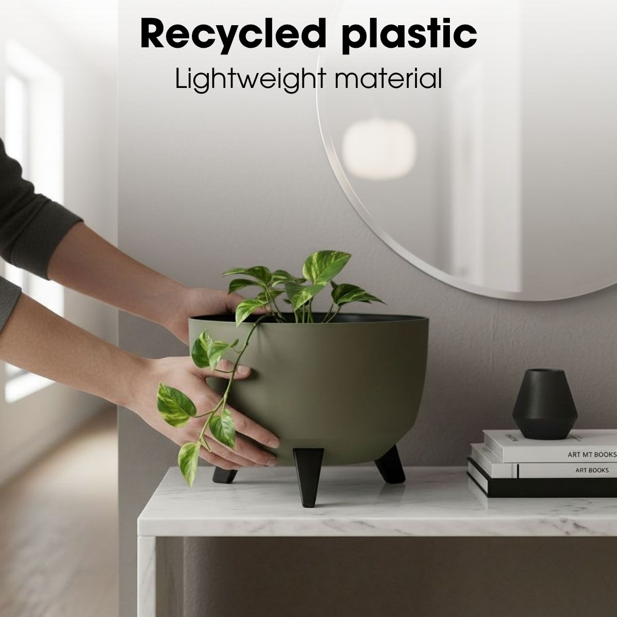 Une personne place un pot vert avec une plante sur une table en marbre blanc à côté de livres.