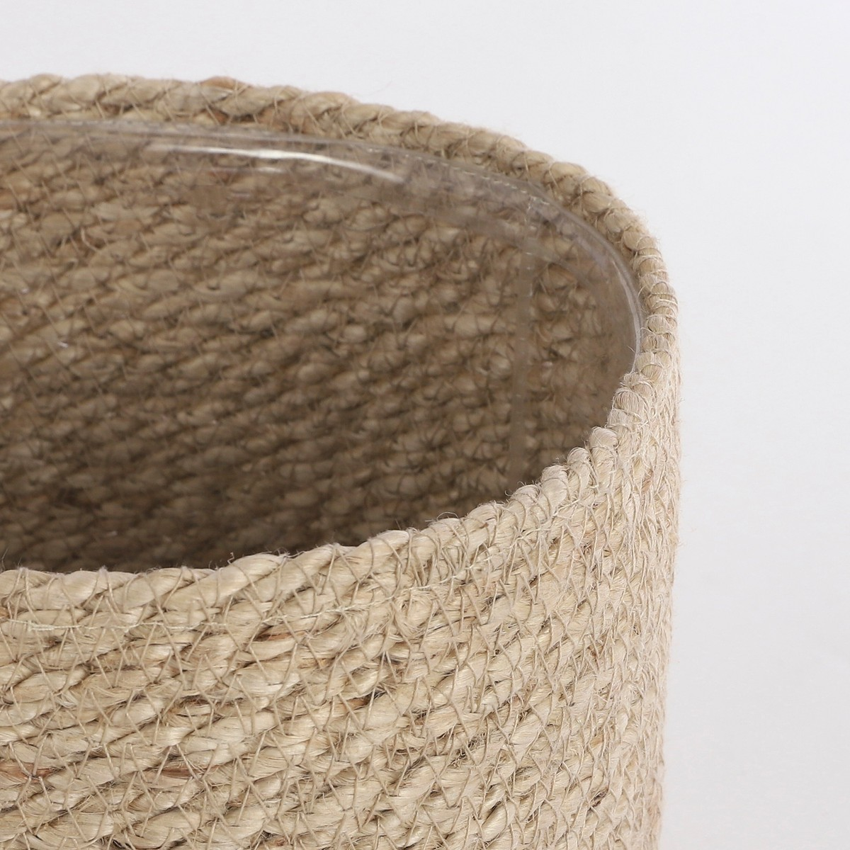Gros plan sur un panier en jute tressé doublé de plastique transparent, sur fond blanc.