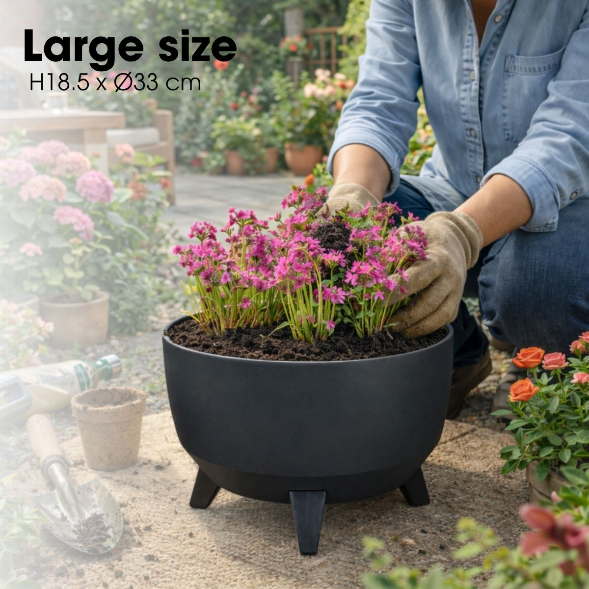Personne en tenue de jardinage plantant des fleurs roses dans un pot noir.