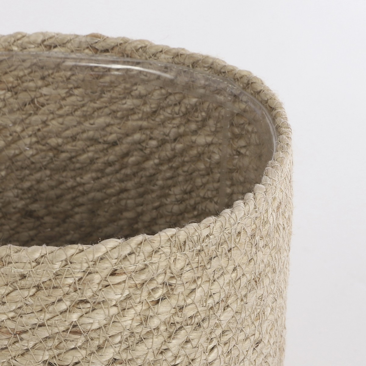 Gros plan d'un pot de fleurs en jute tressé avec un insert en verre transparent sur fond blanc.