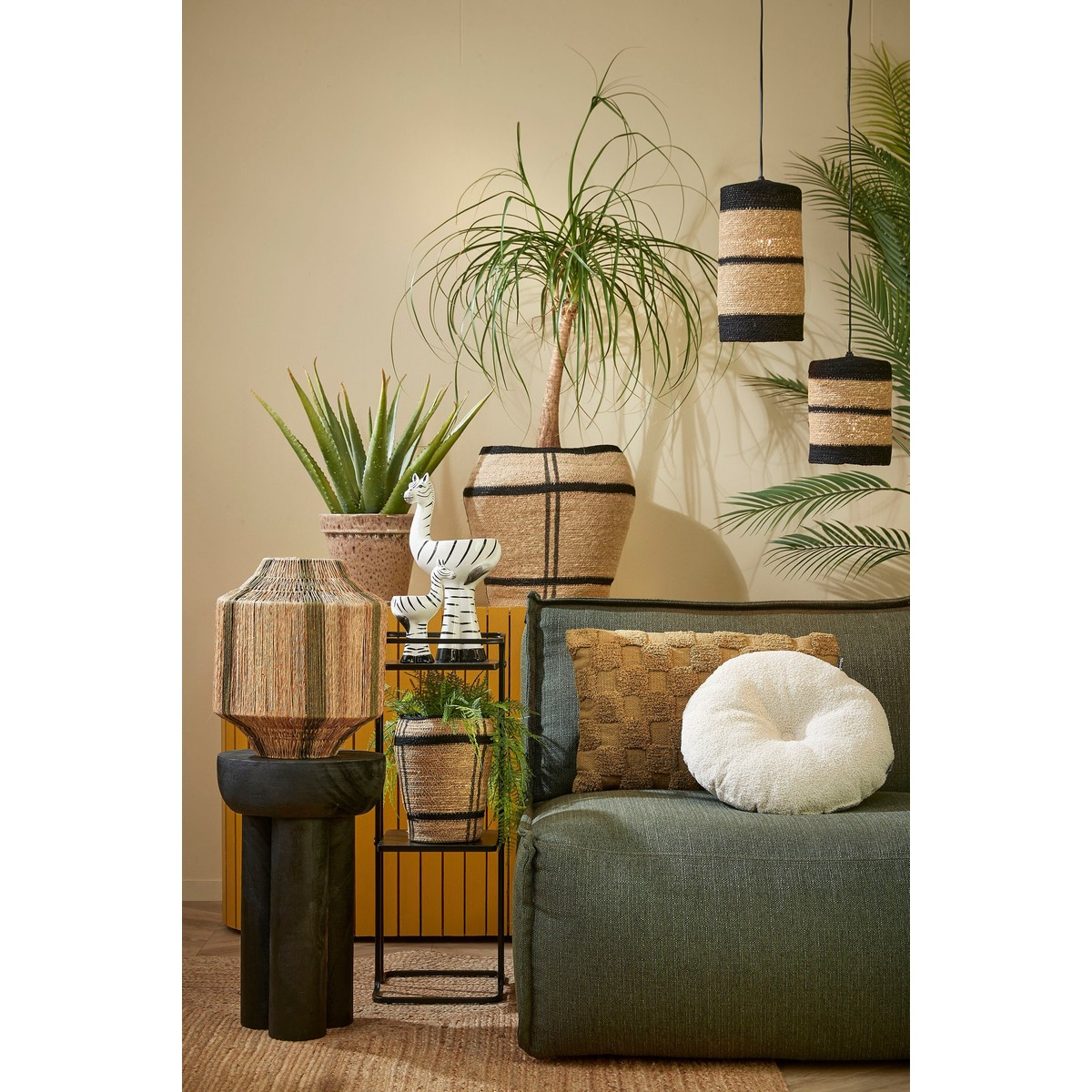 Groene bank met kussens, planten, zebrabeeldje en zwart-beige hanglampen.