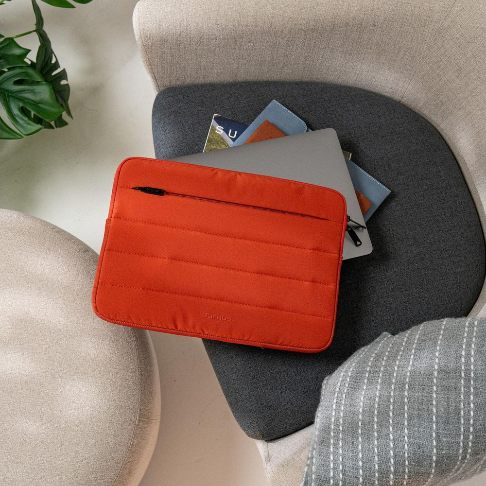 Eine orangefarbene Laptoptasche liegt auf einem grauen Sessel neben Notizbüchern und einem Laptop.