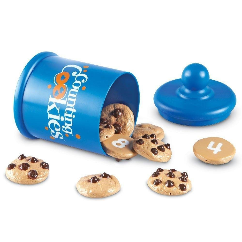 Blaue Keksdose mit der Aufschrift Counting Cookies und Plastikkekse mit Schokostücken und Zahlen liegen auf weißem Hintergrund.