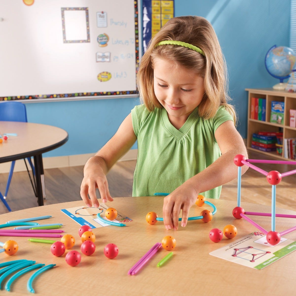 Ein junges Mädchen baut im Klassenzimmer Formen mit bunten Stäben und Kugeln.