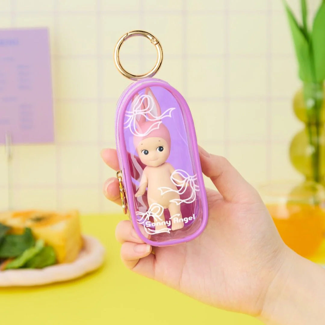 Eine Hand hält eine kleine, lila Tasche mit einem kleinen Engels-Figur darin.