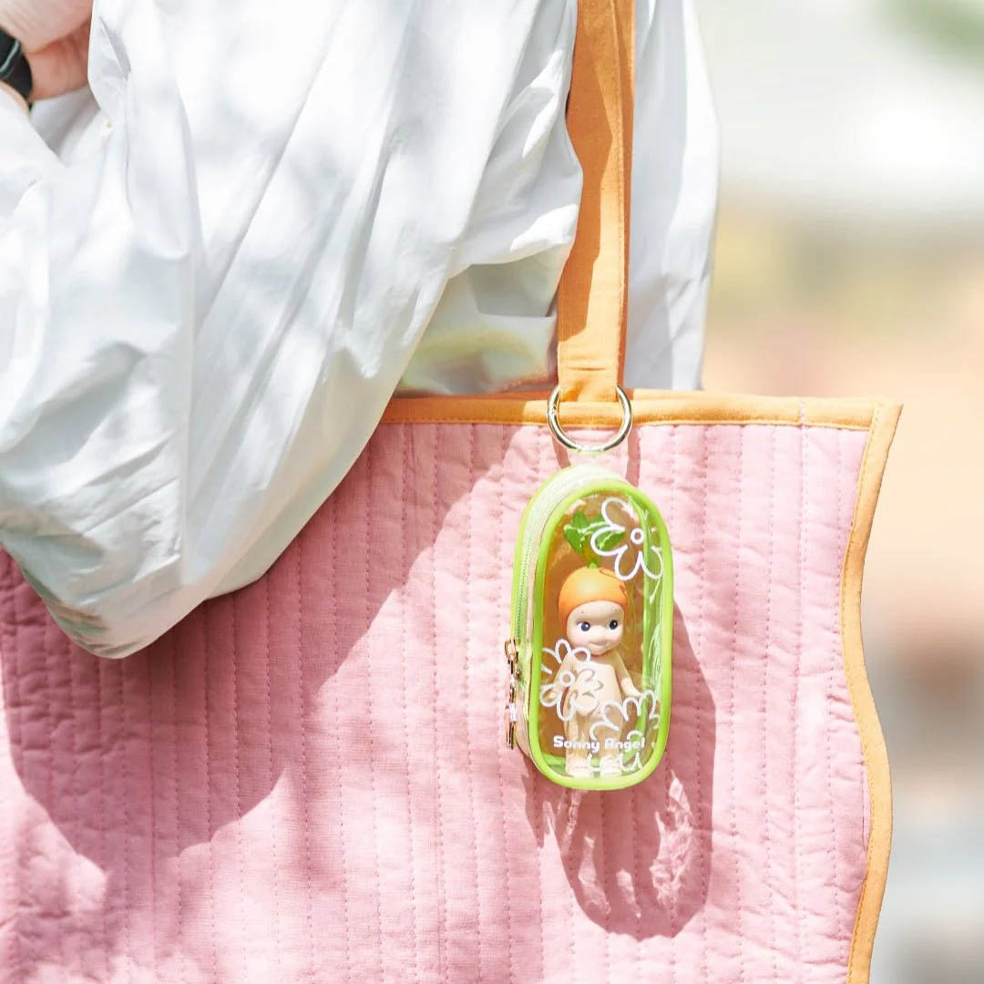 Eine pinke gesteppte Tasche mit orangefarbenem Rand hängt an einer Schulter, mit einer grünen transparenten Tasche.