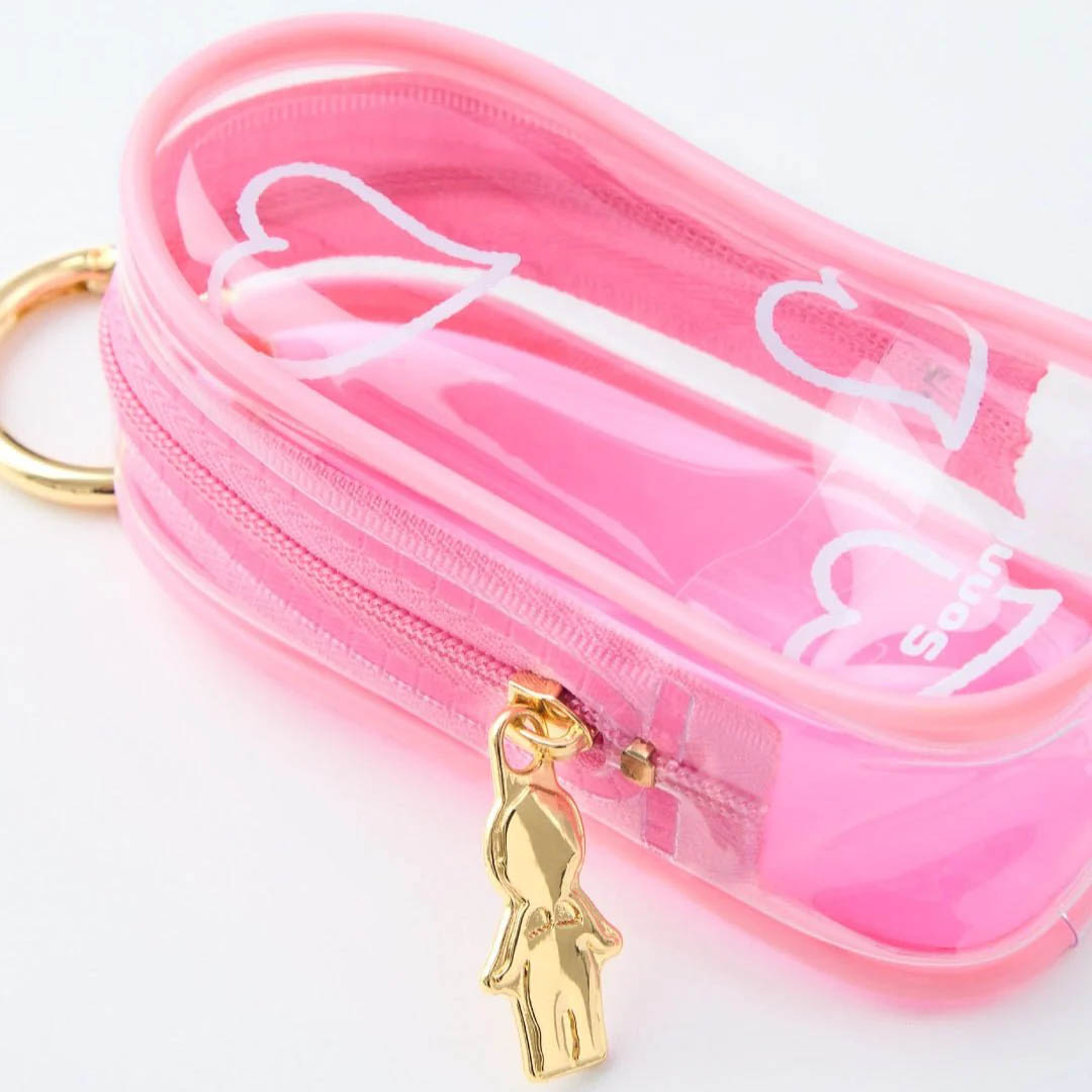 Ein rosa, transparenter, ovaler Beutel mit einem goldenen Reißverschluss und einem goldenen puppenförmigen Anhänger.